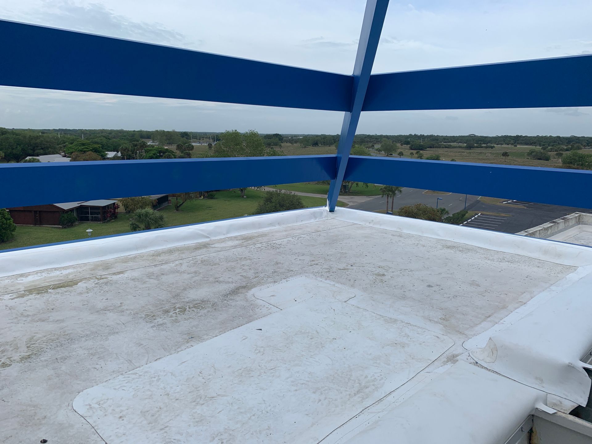 Rooftop with blue railings overlooking distant buildings and greenery under a clear sky