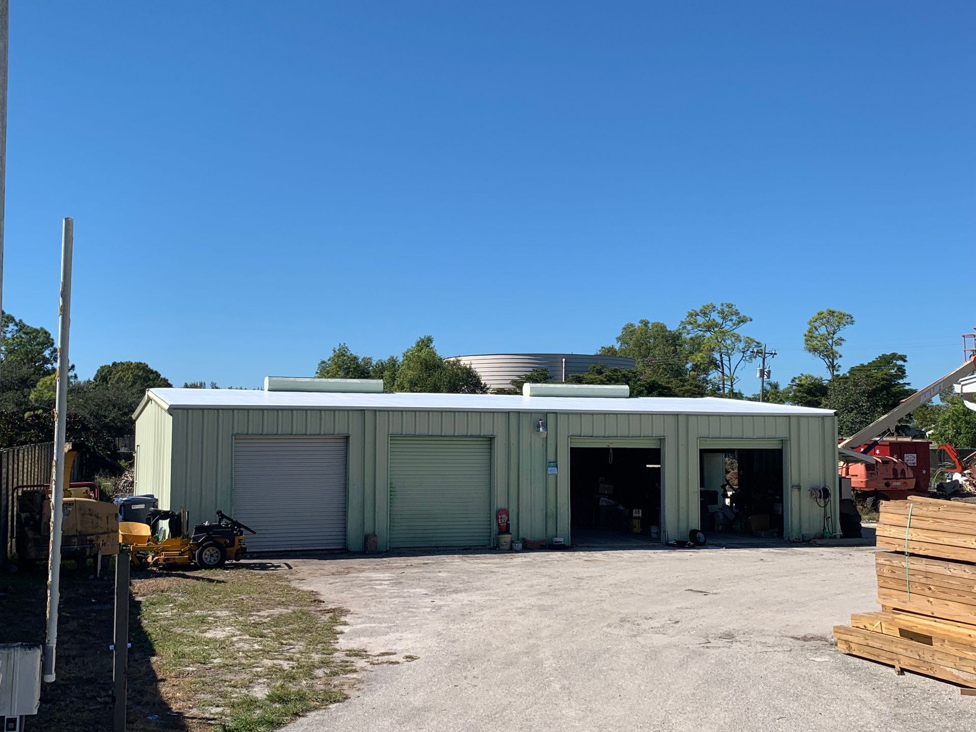 Industrial warehouse with white metal siding and open garage bays on a gravel lot under a clear blue sky