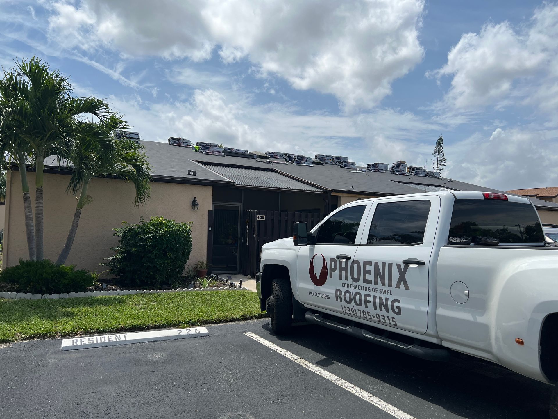 White Phoenix Roofing pickup parked outside a beige house with a damaged roof under a cloudy sky