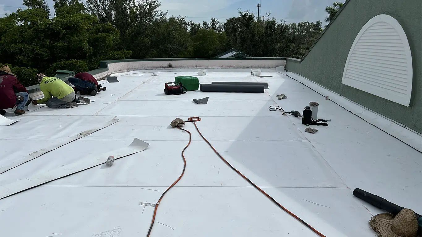 White flat roof under repair with tools, buckets, and workers near the edges