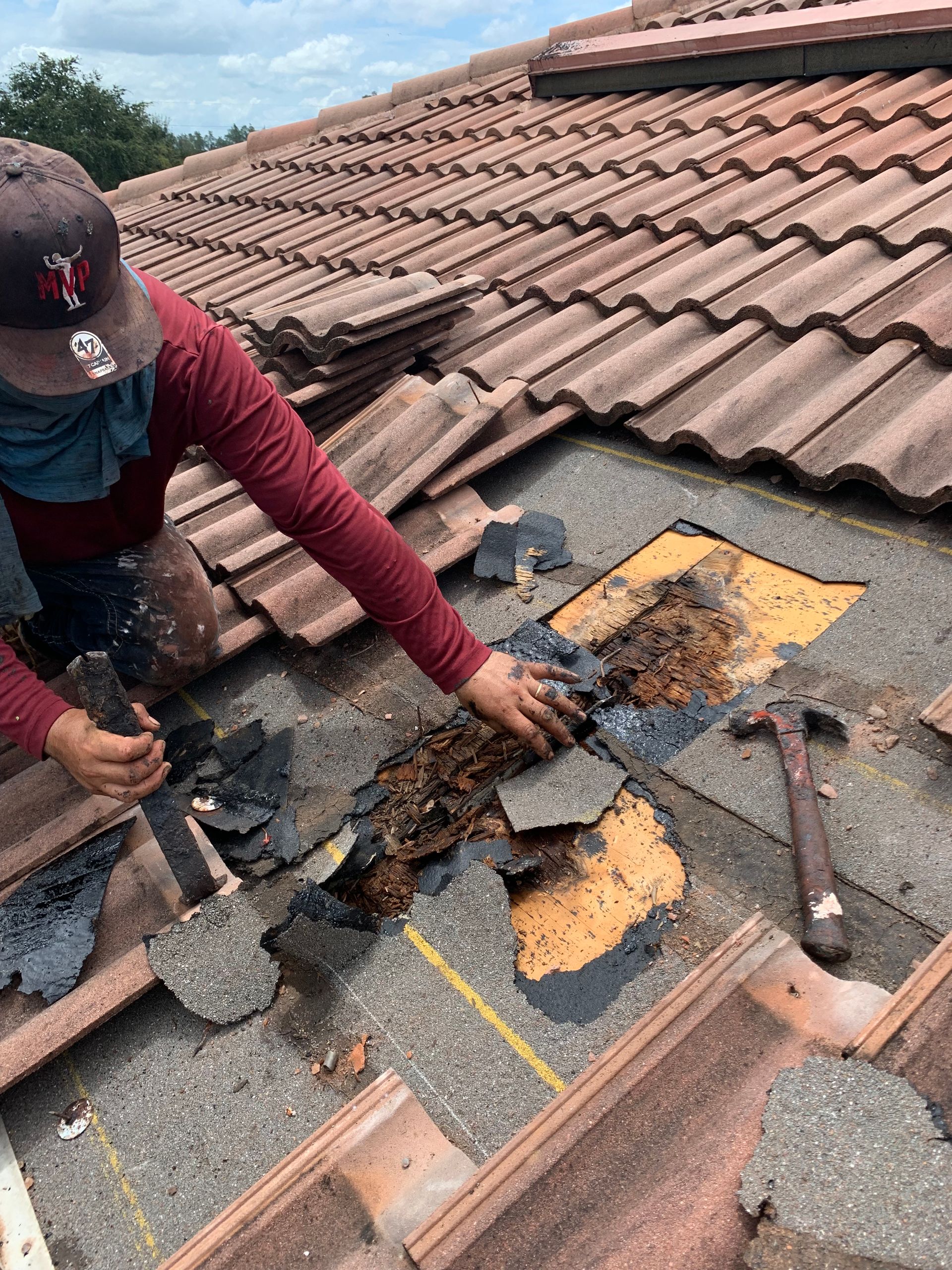 Person repairing a damaged roof section with tools and exposed underlayment