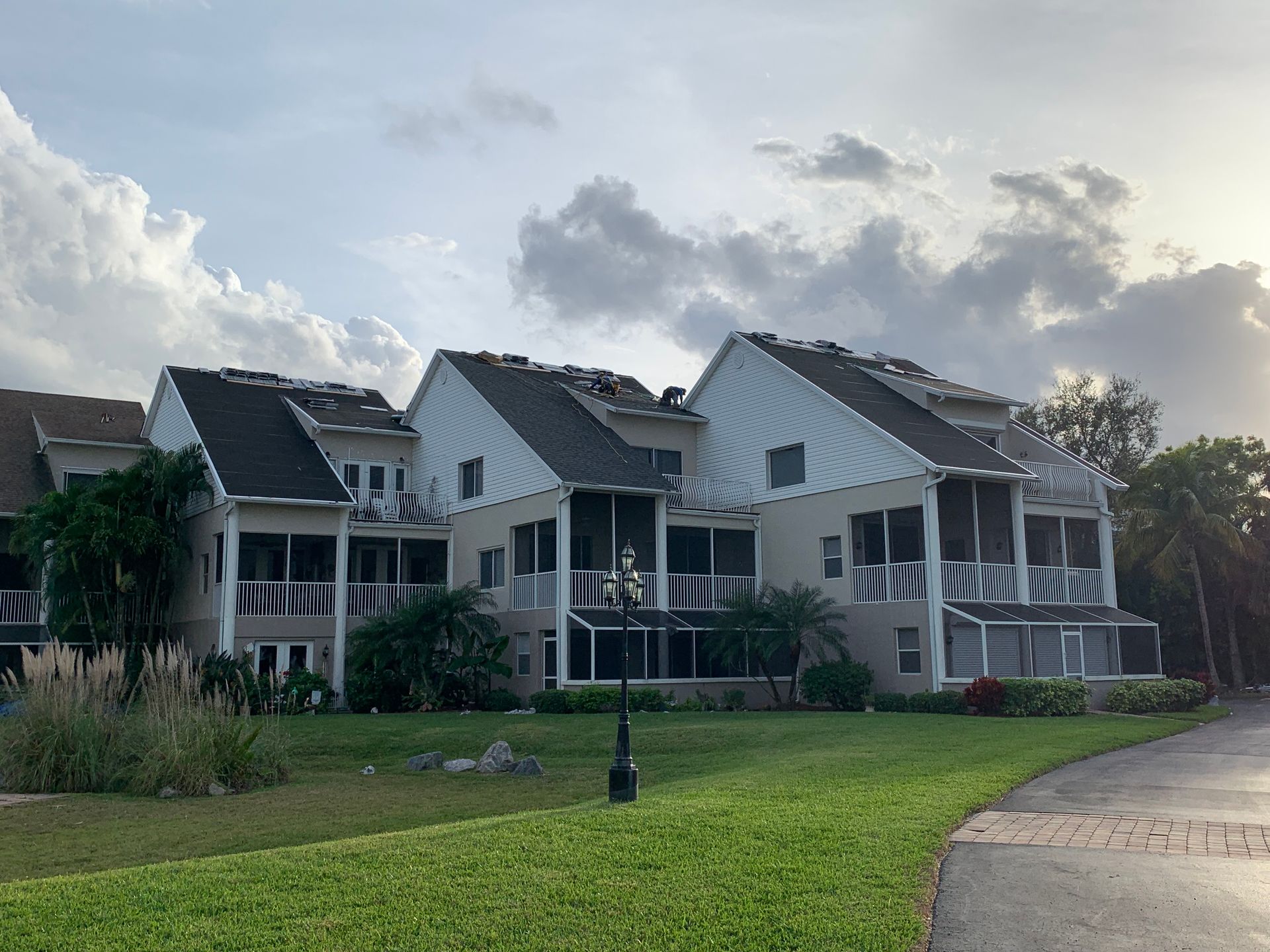 Row of white houses with dark roofs beside a green lawn under a cloudy sky