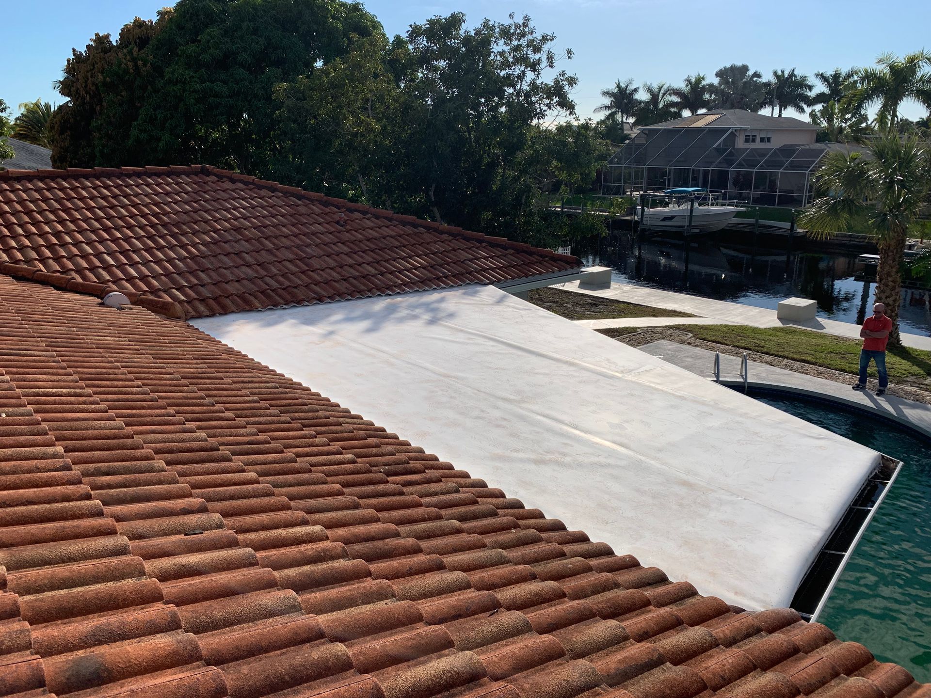 Tiled roof with a large white tarp, by a canal with trees and a person standing near the edge