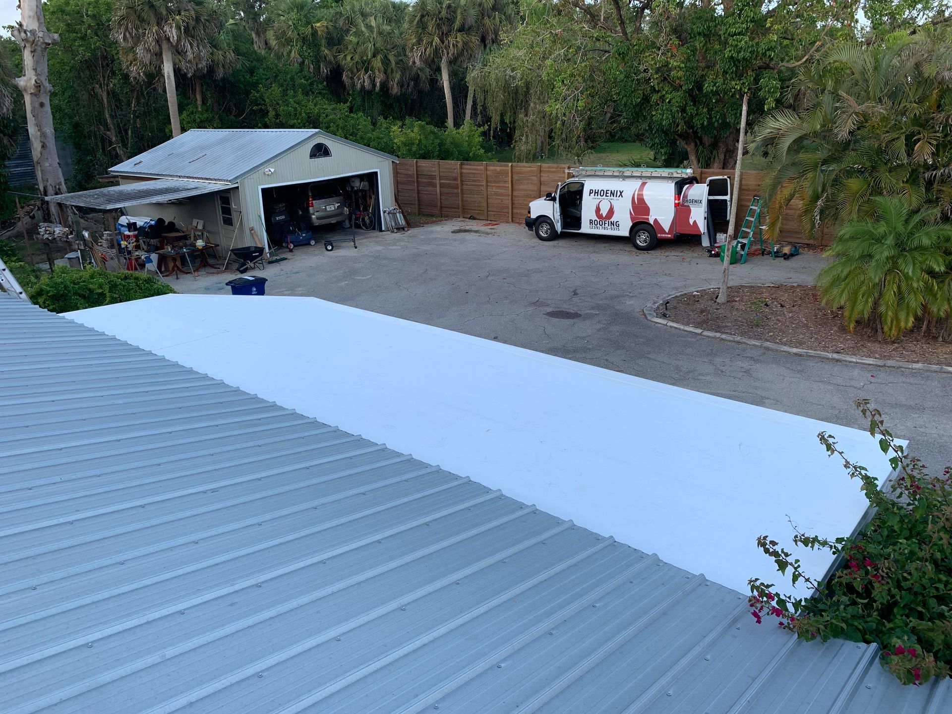 White roof under construction beside a garage, with a work van and trees in the background.