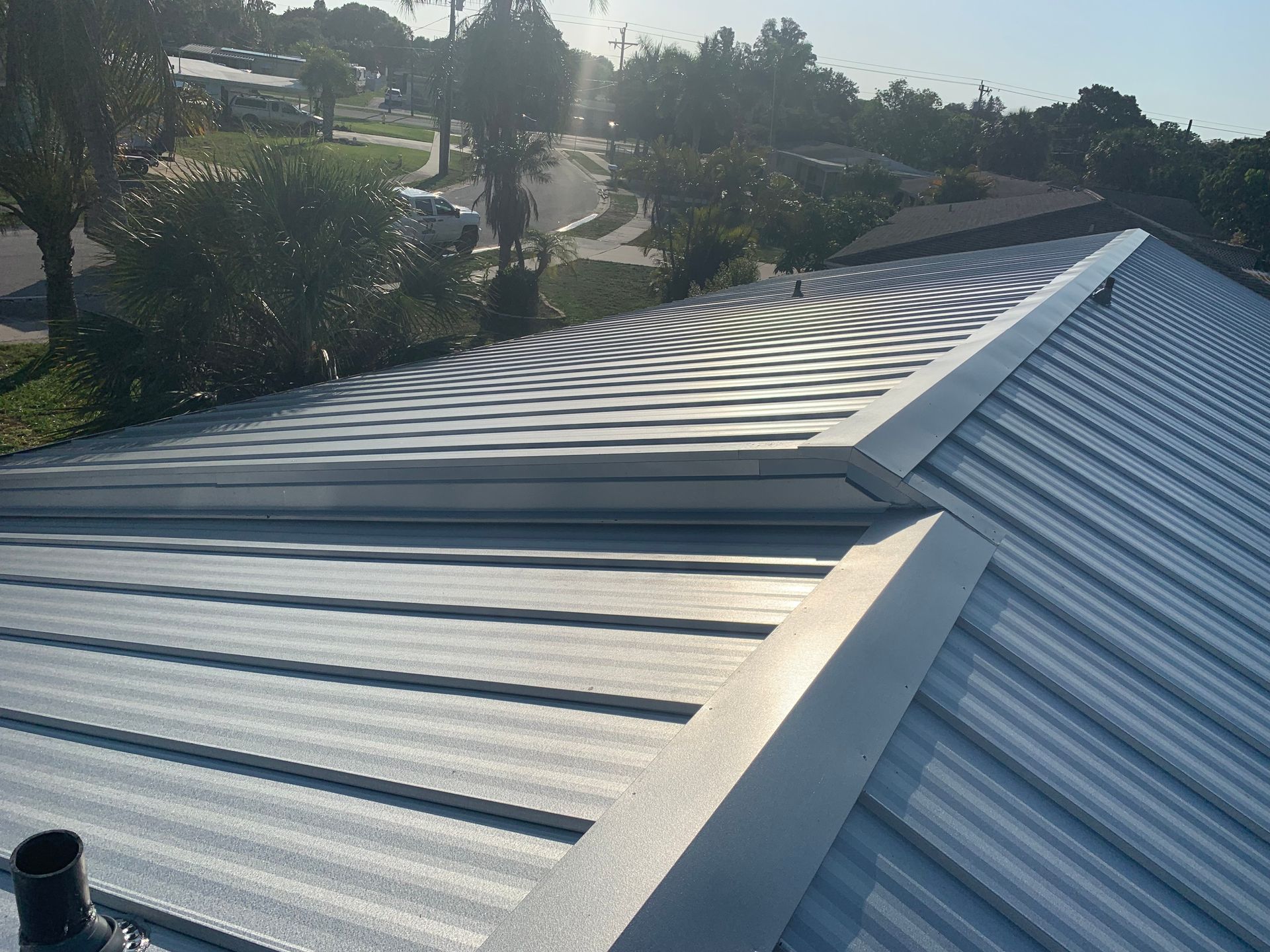 Metal roof under construction with ridged panels and a bright sky above landscaping in the background