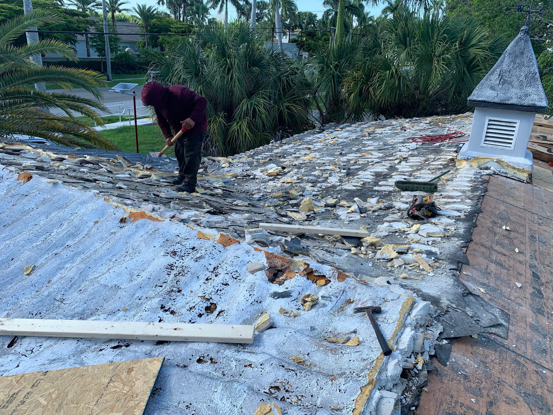 Worker inspecting a damaged roof with broken shingles and debris beside a white vent structure