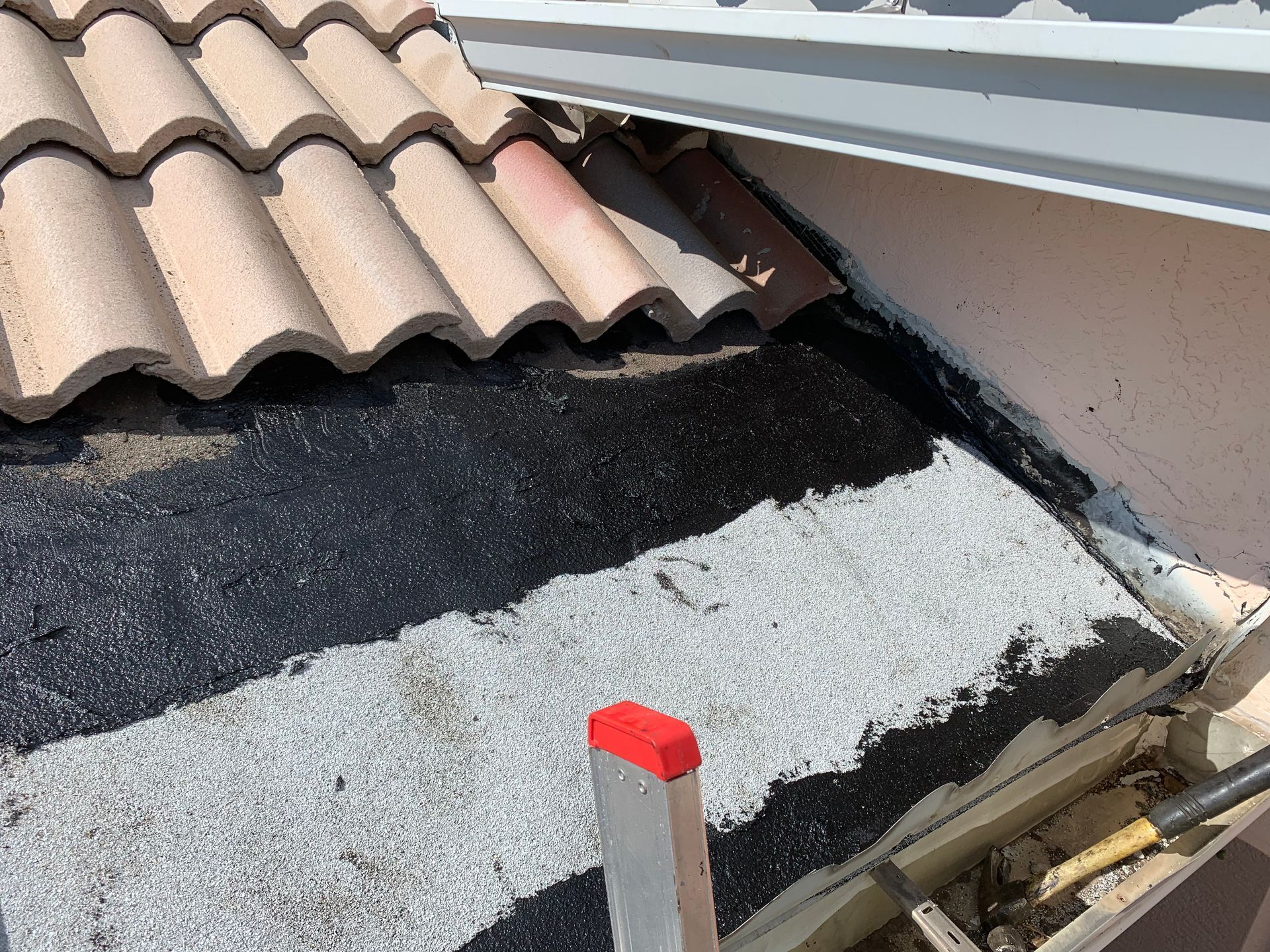 Roof repair with exposed black underlayment beside gray tiles and a rooftop vent pipe with a red cap
