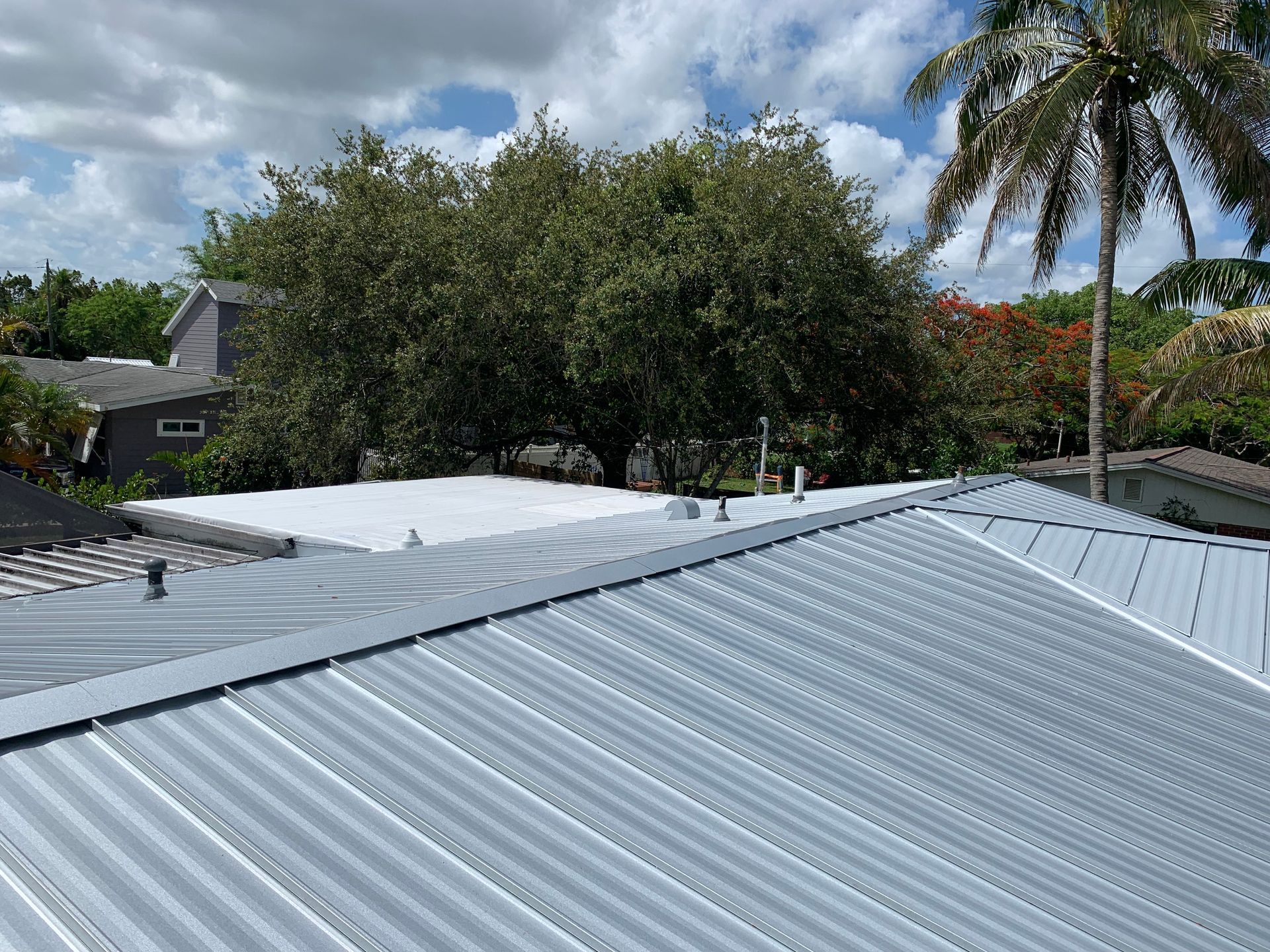 Corrugated metal roof with trees and a partly cloudy sky in the background