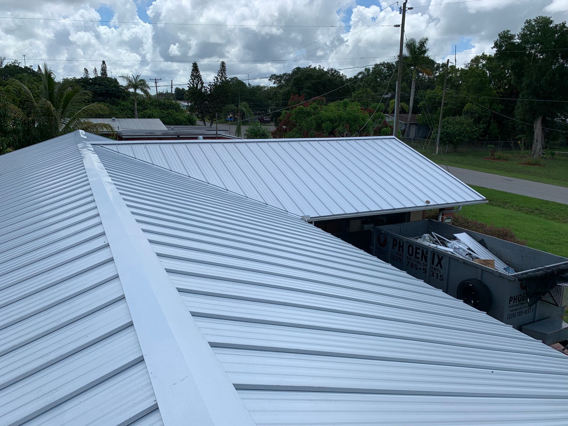 White corrugated metal roof on a house with a cloudy sky and trees in the background