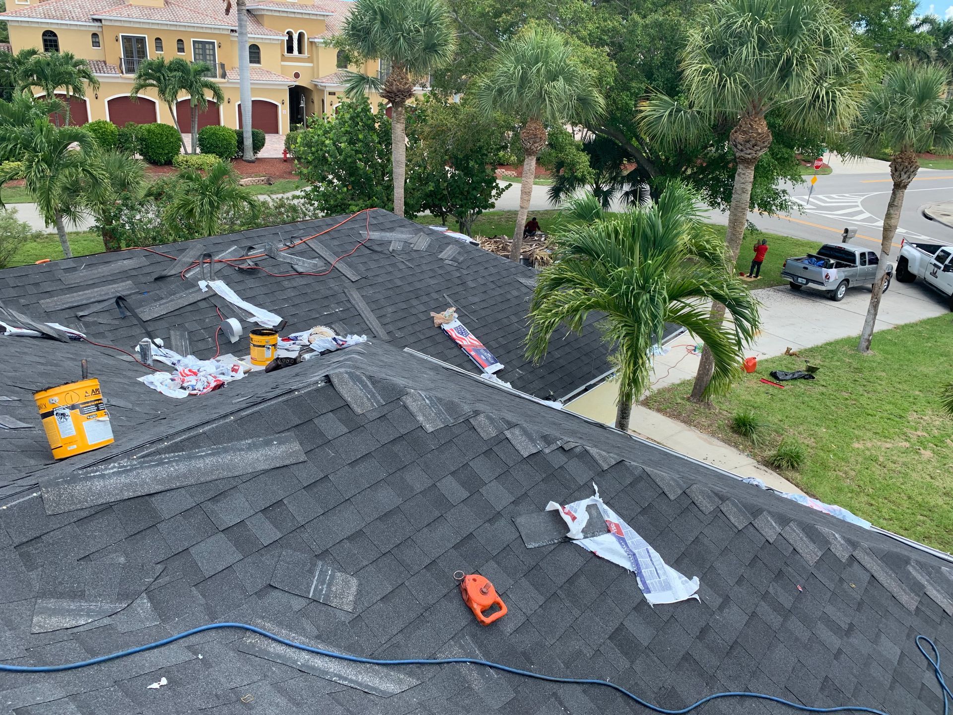 Roof with dark shingles and scattered tools, viewed from above near trees and parked cars