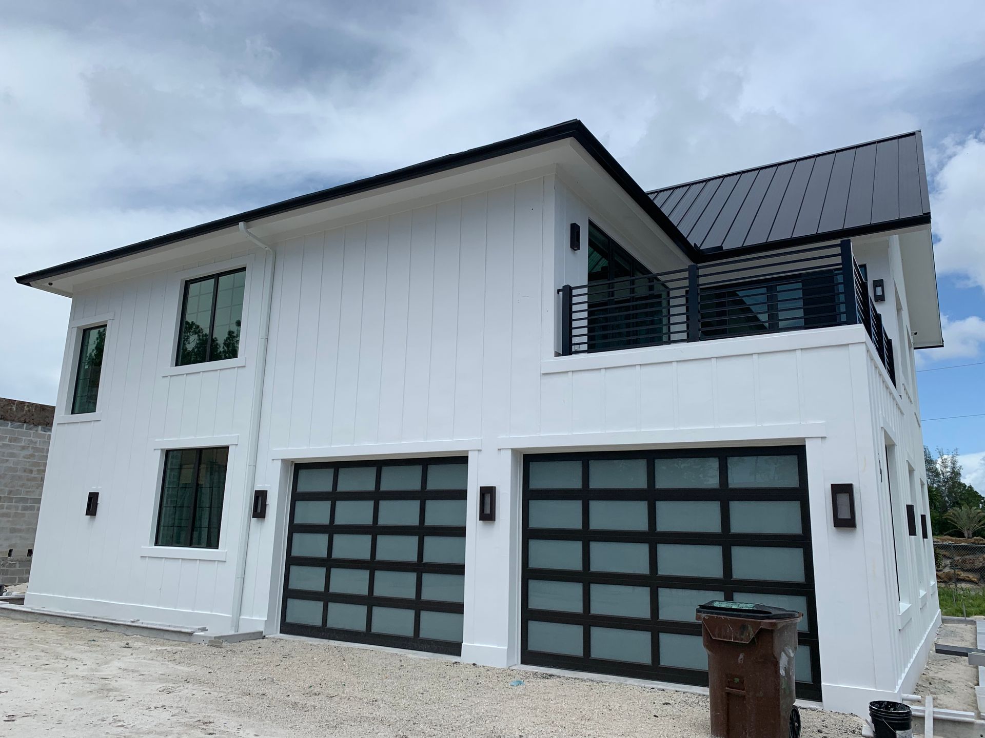 Modern white two-story house with black roof and double garage doors under cloudy sky