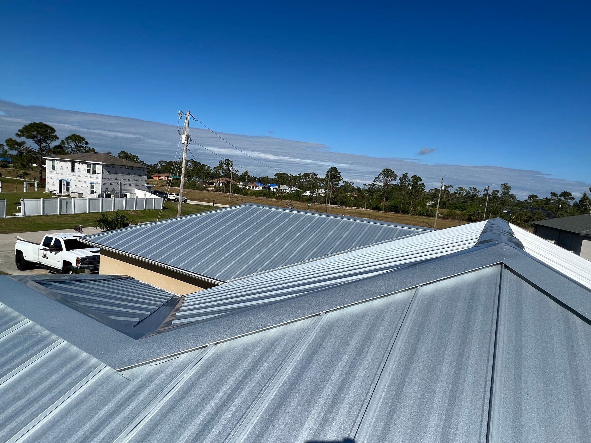 Silver corrugated metal rooftops with a white truck, houses, and hills under a clear blue sky