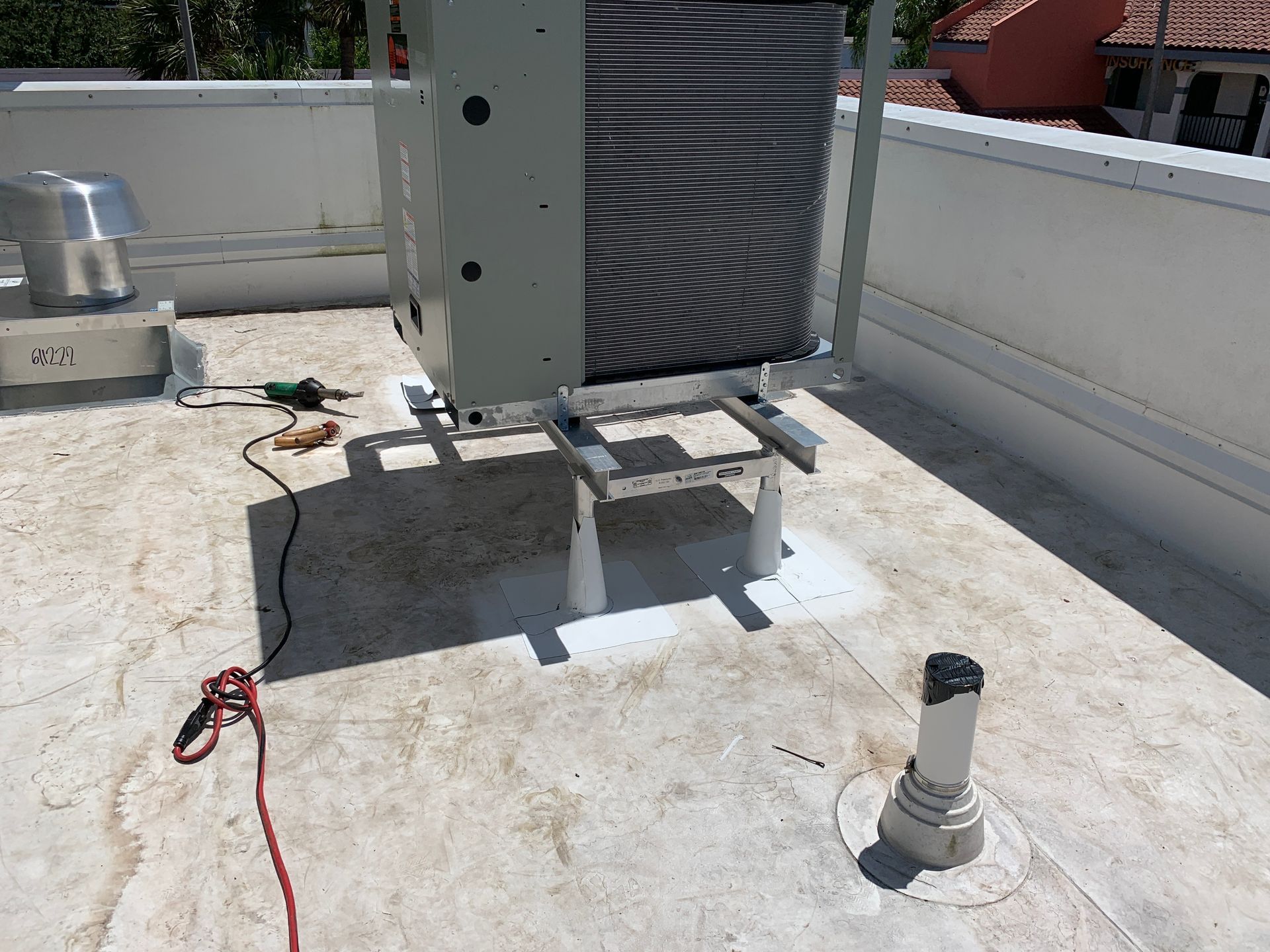 Roof equipment on a flat rooftop, with a large gray HVAC unit, cables, and a white vent pipe.