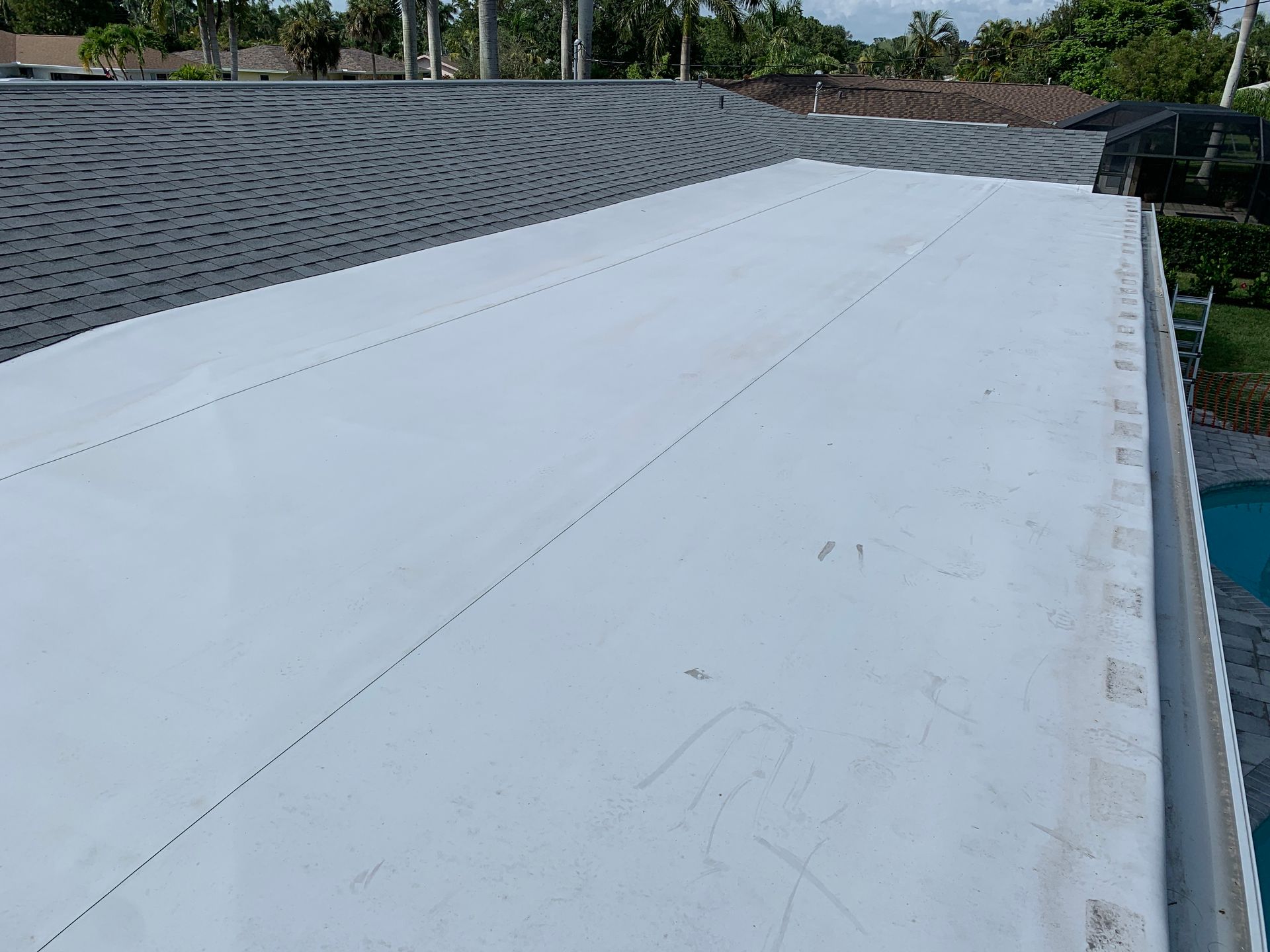 Flat white rooftop membrane beside a sloped gray shingle roof and blue pool edge outdoors