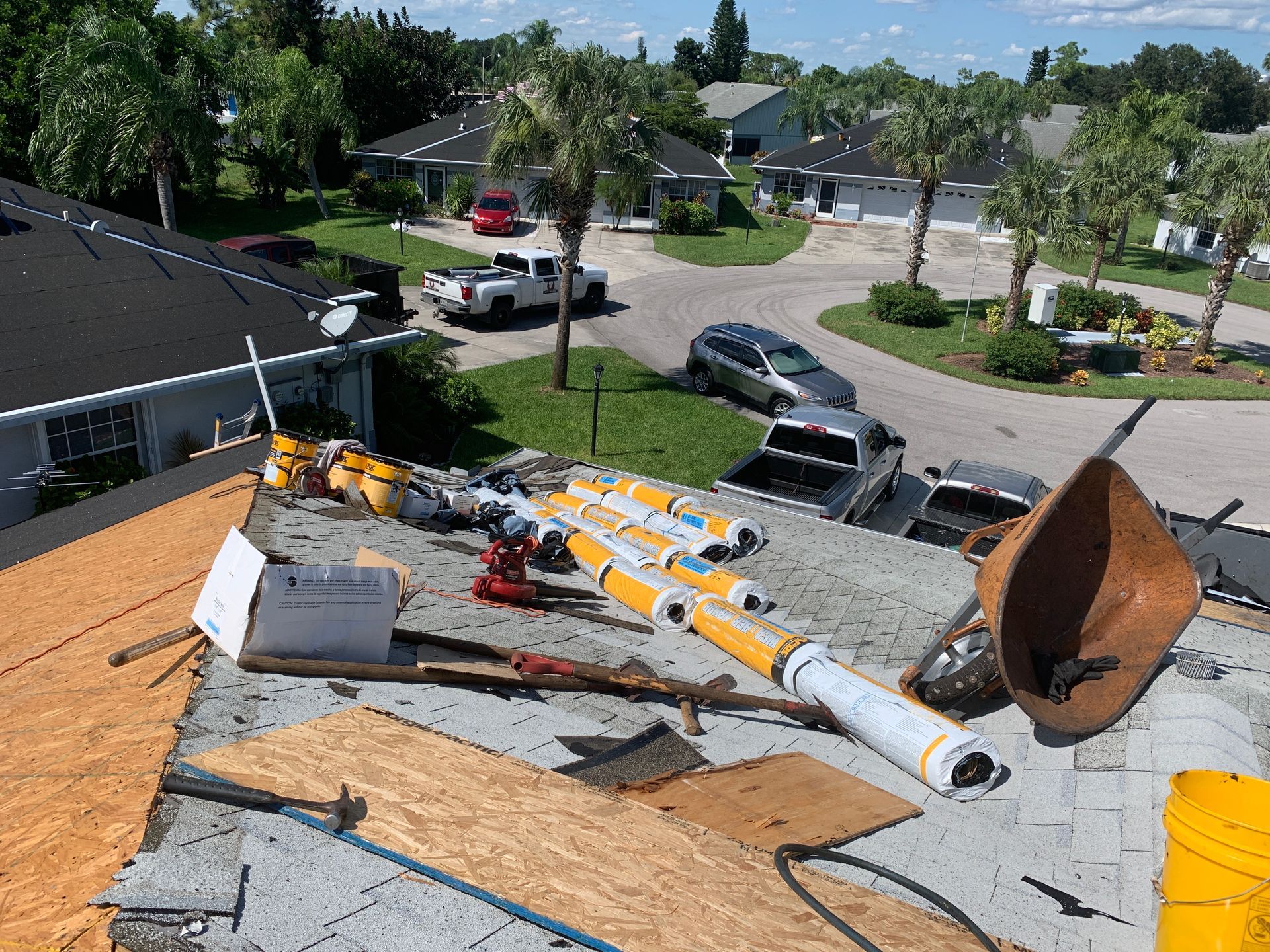 Roof with construction debris and tools scattered on shingles, viewed over a suburban neighborhood.