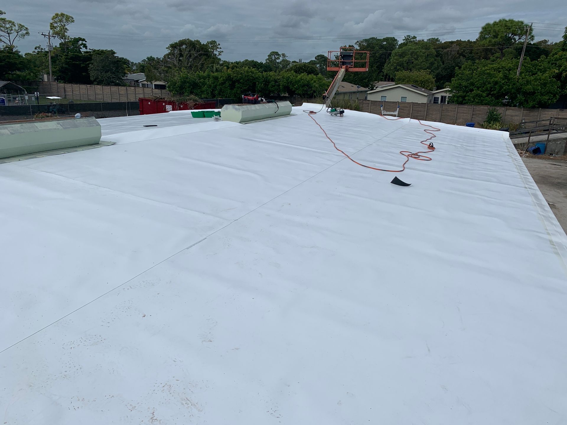 White rooftop under construction with a red safety line and cloudy sky in the background