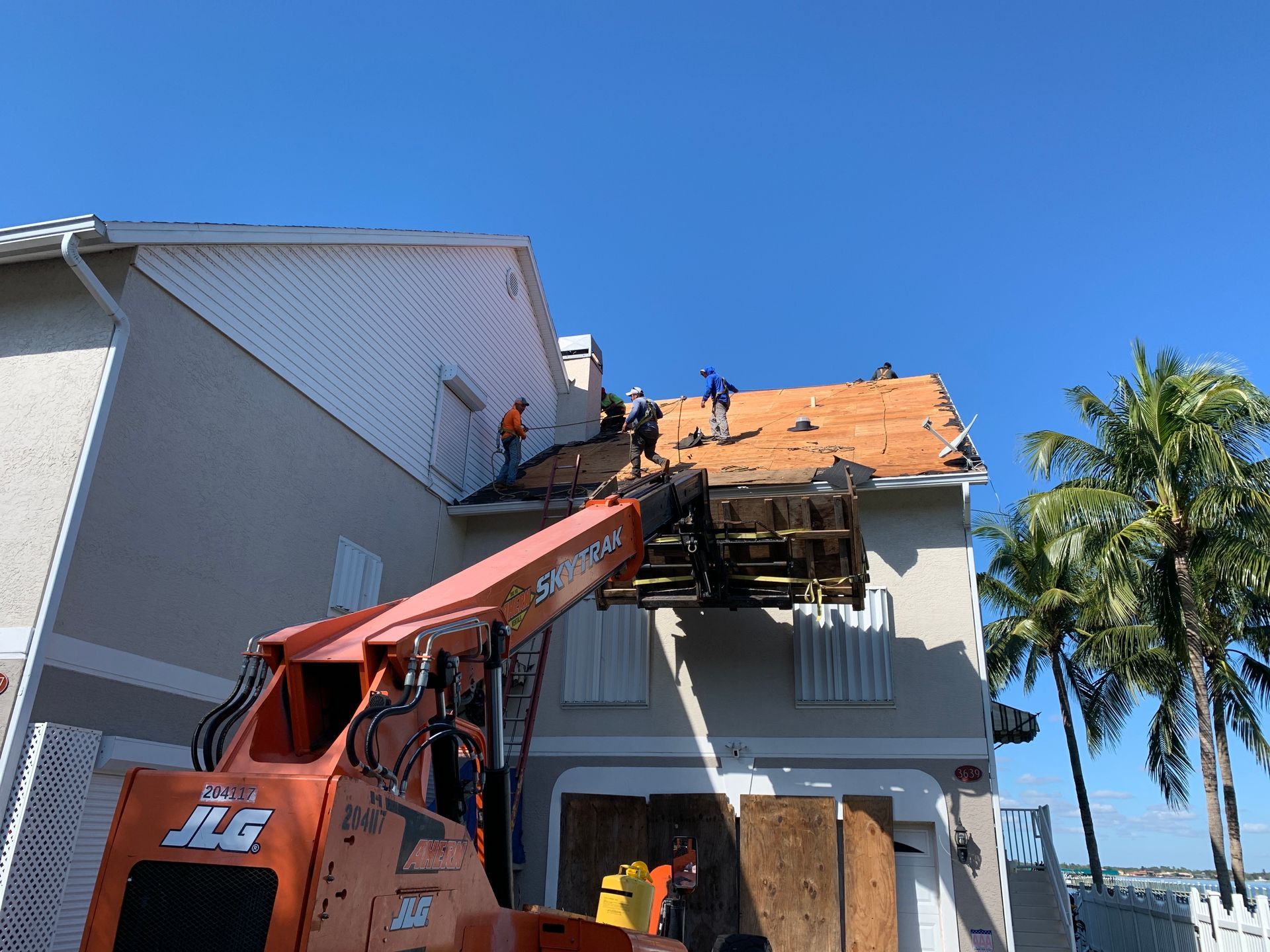 Roofing crew using a boom lift to replace shingles on a house under a blue sky