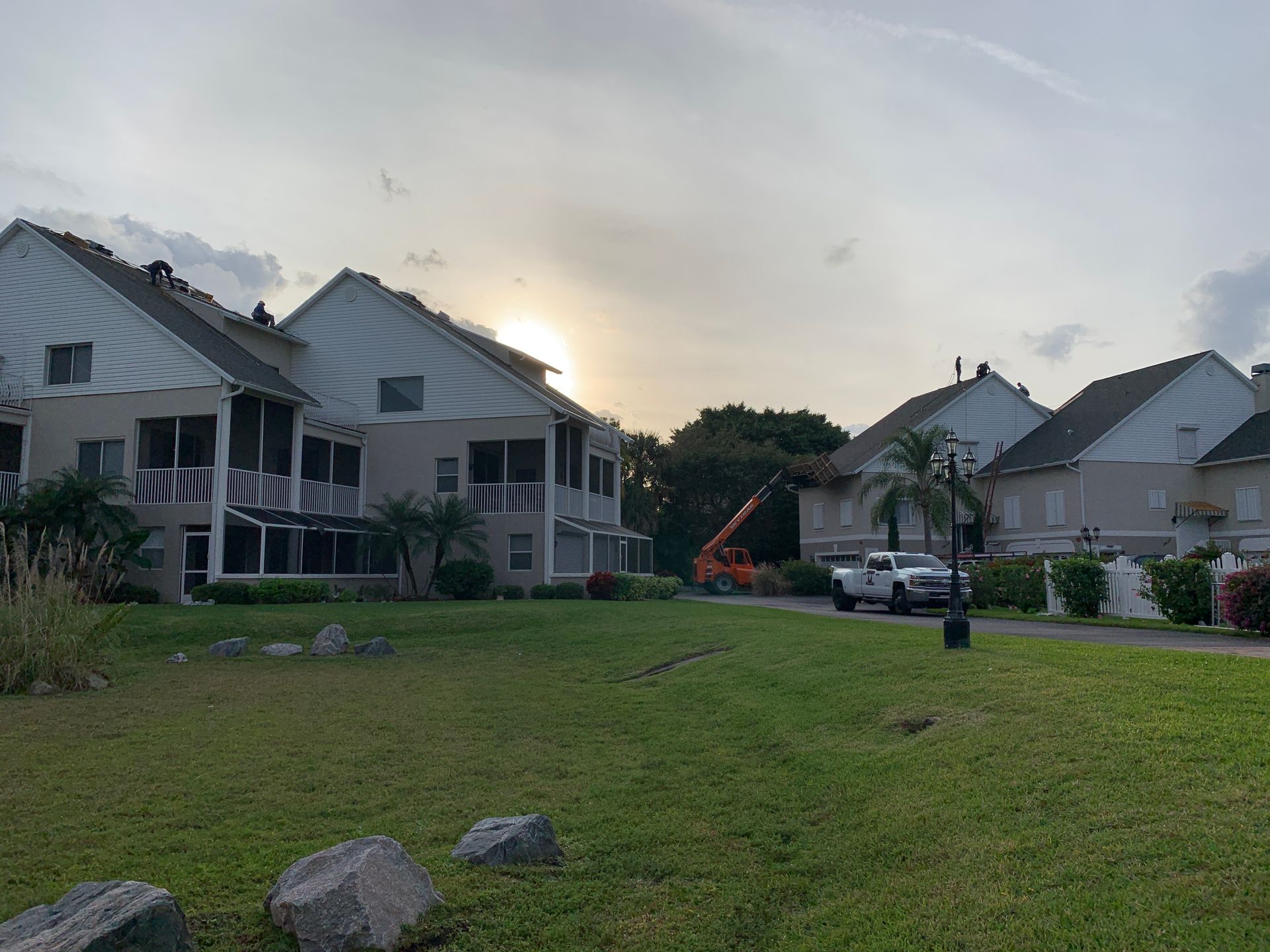 Row of townhouses at sunset with a grassy lawn, parked cars, and an orange excavator in the background