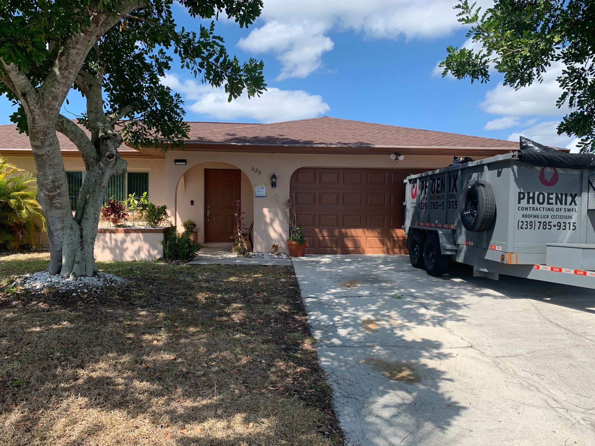 Single-story house with a brown roof, arched entry, tree in front, and a parked Phoenix waste truck in the driveway