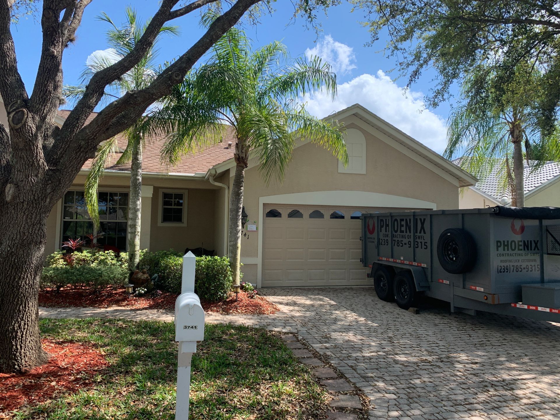 Suburban house with two-car garage and a utility trailer parked in the driveway under trees