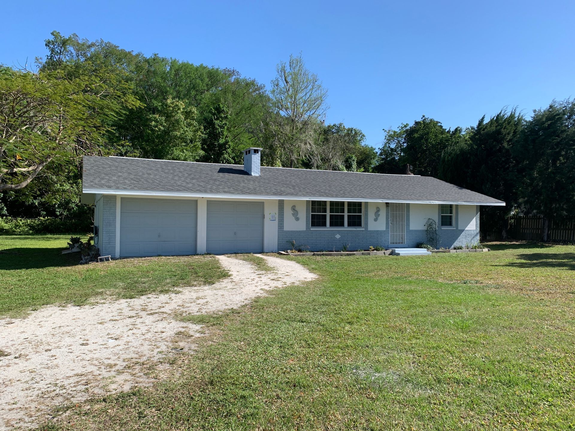 Single-story white house with two garage doors and a gravel driveway on a grassy lot.