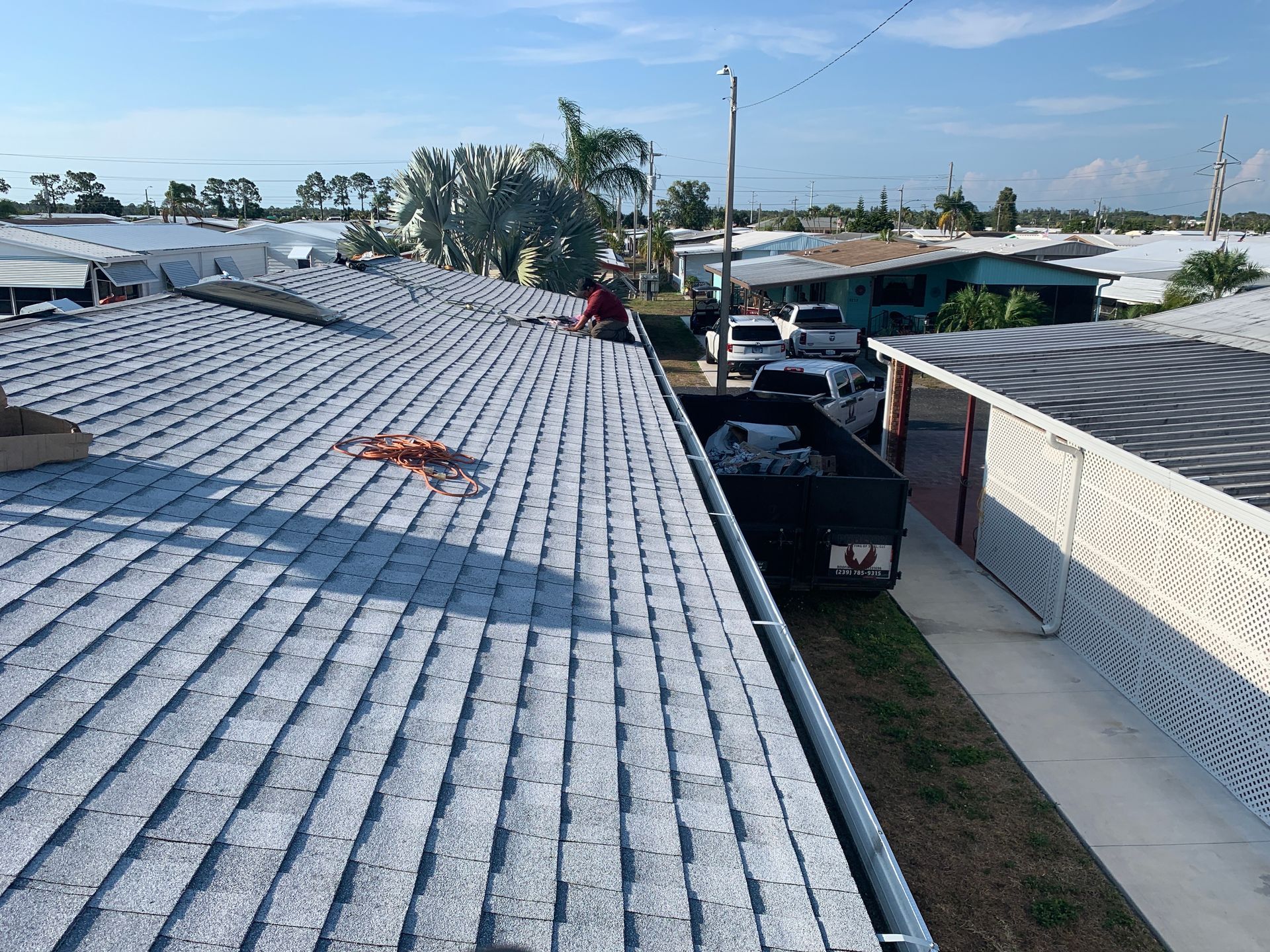 Rooftop view of white corrugated roofs, a narrow alley, and parked trucks under a blue sky.