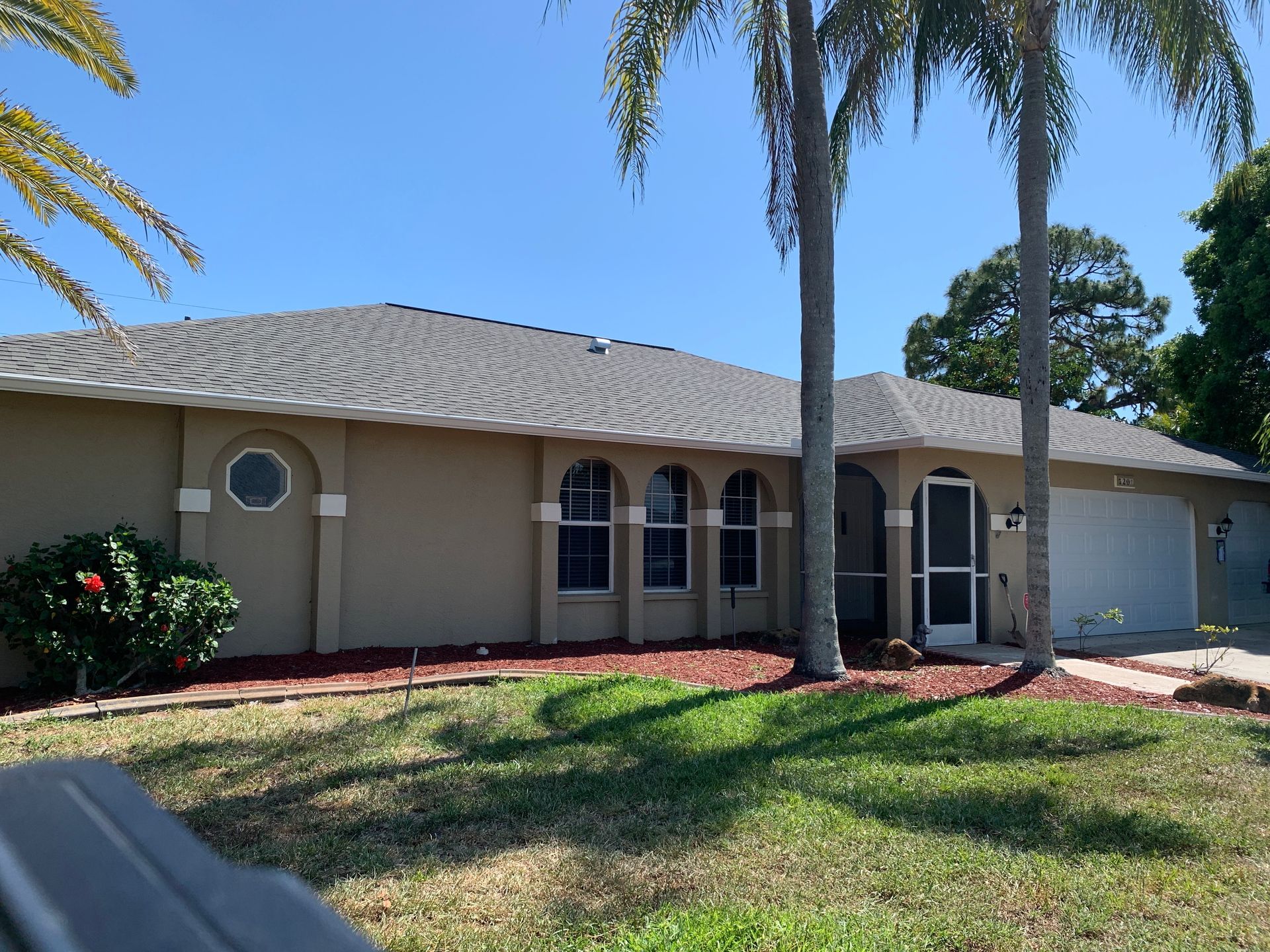 Single-story tan house with arched windows, palm trees, and a sunny front lawn