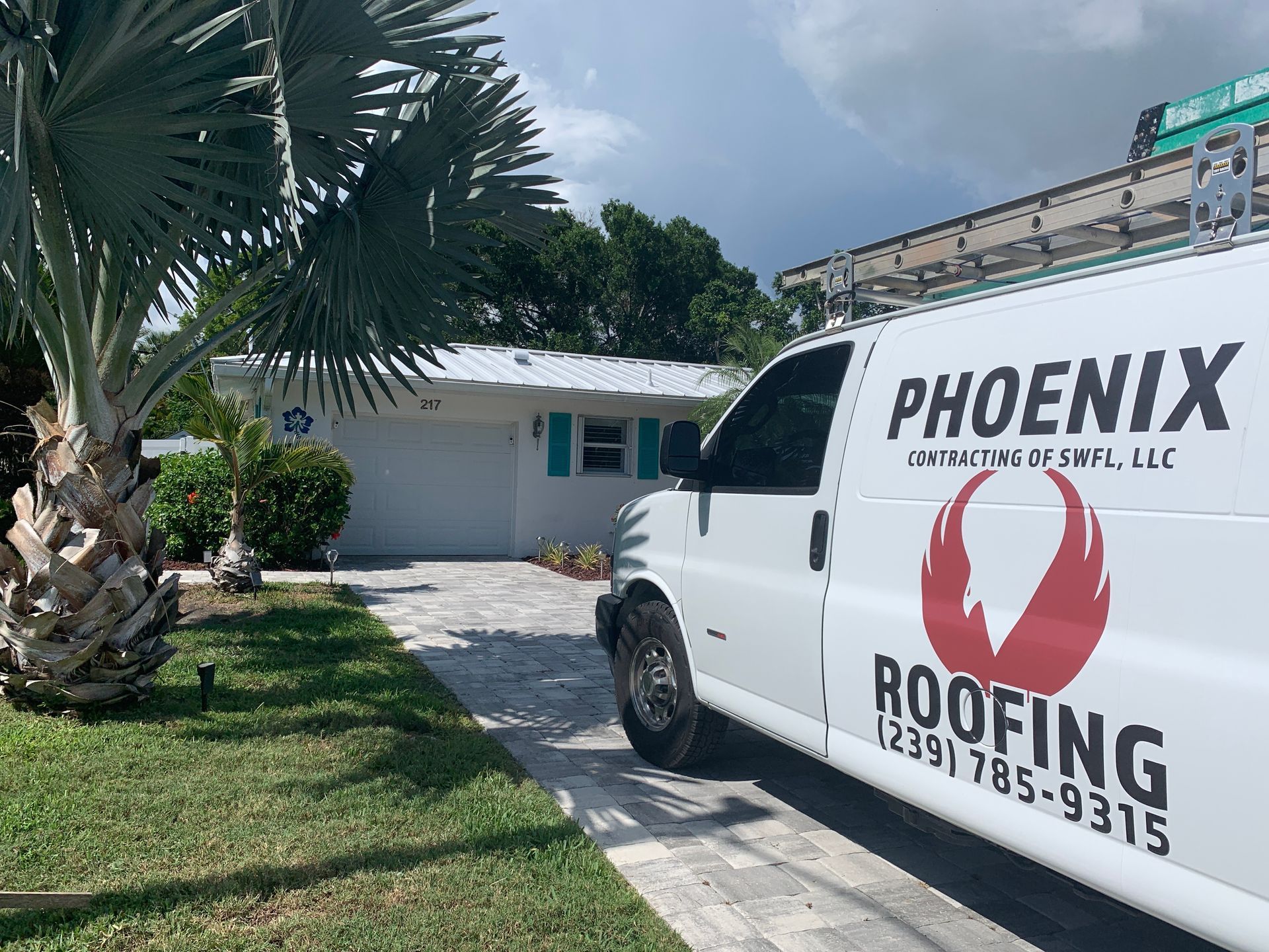 White Phoenix Roofing van parked by a house with palm trees and a roof ladder on top