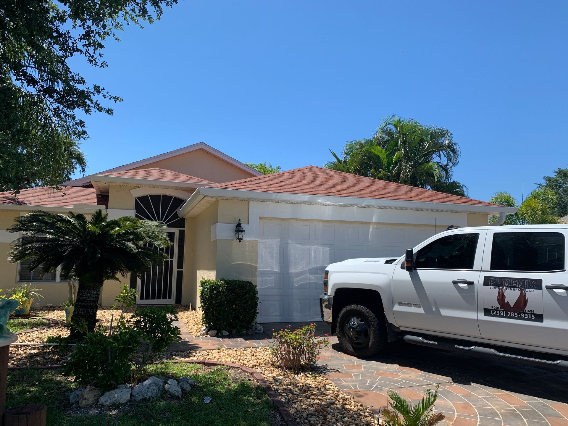 White pickup truck parked in front of a beige house with a red tile roof and palm trees under a blue sky