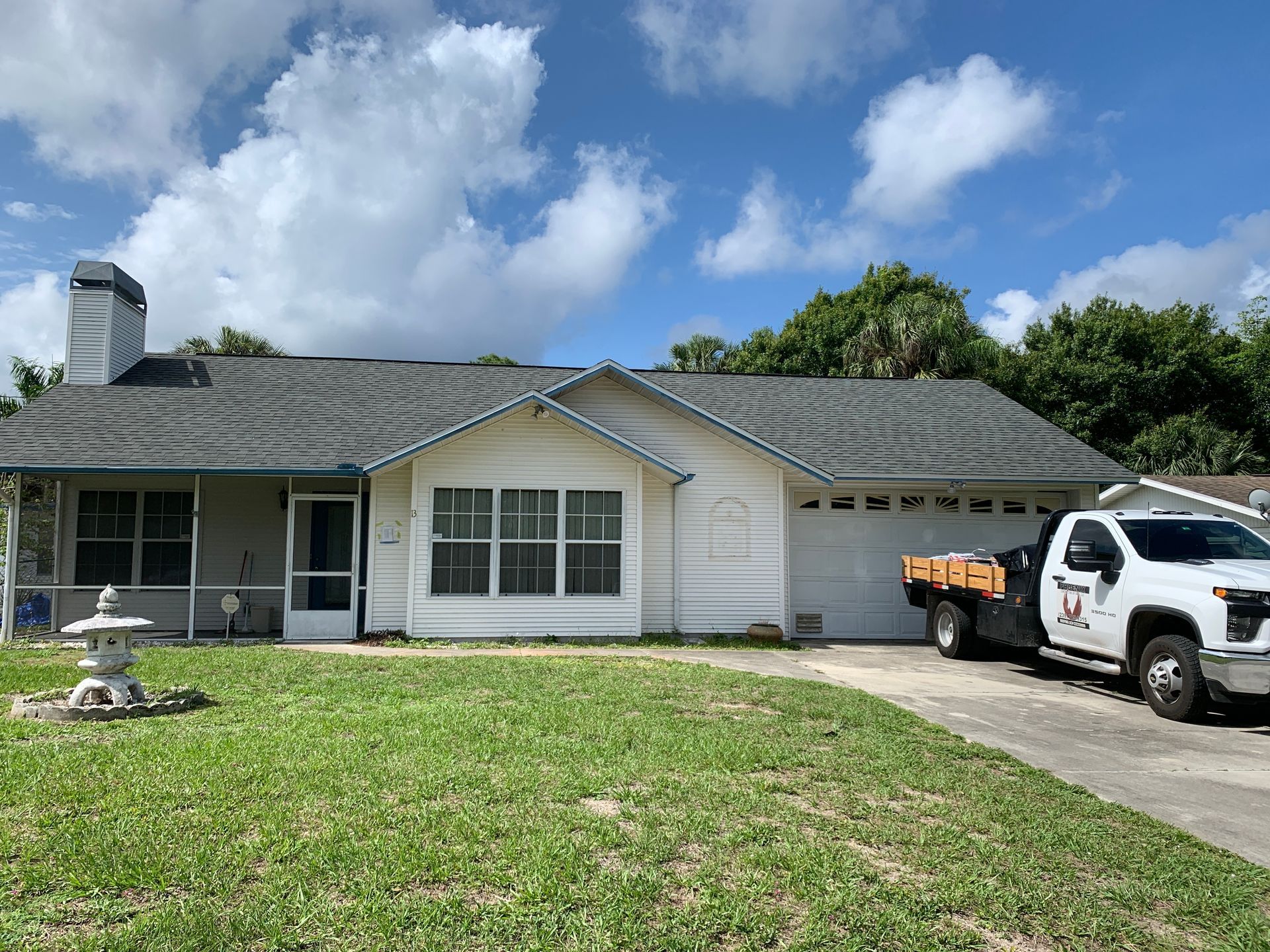 Single-story house with gray roof, white truck in driveway, and green lawn under a partly cloudy sky