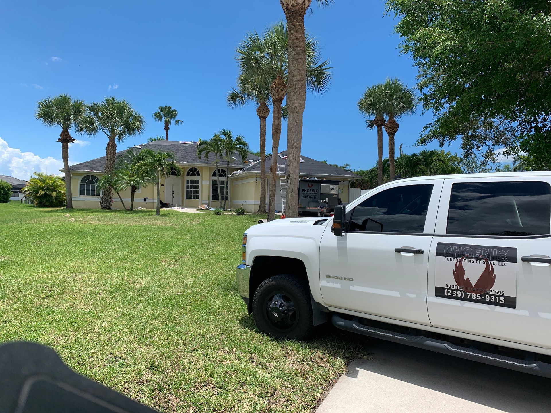 White pickup truck on a grassy lawn in front of a large house with palm trees under a blue sky