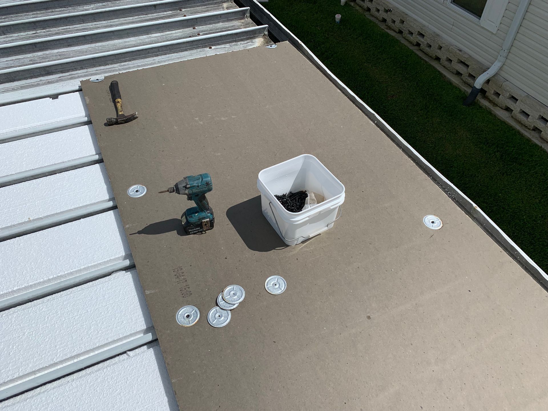 Tools and hardware on a rooftop near a white bucket and scattered washers