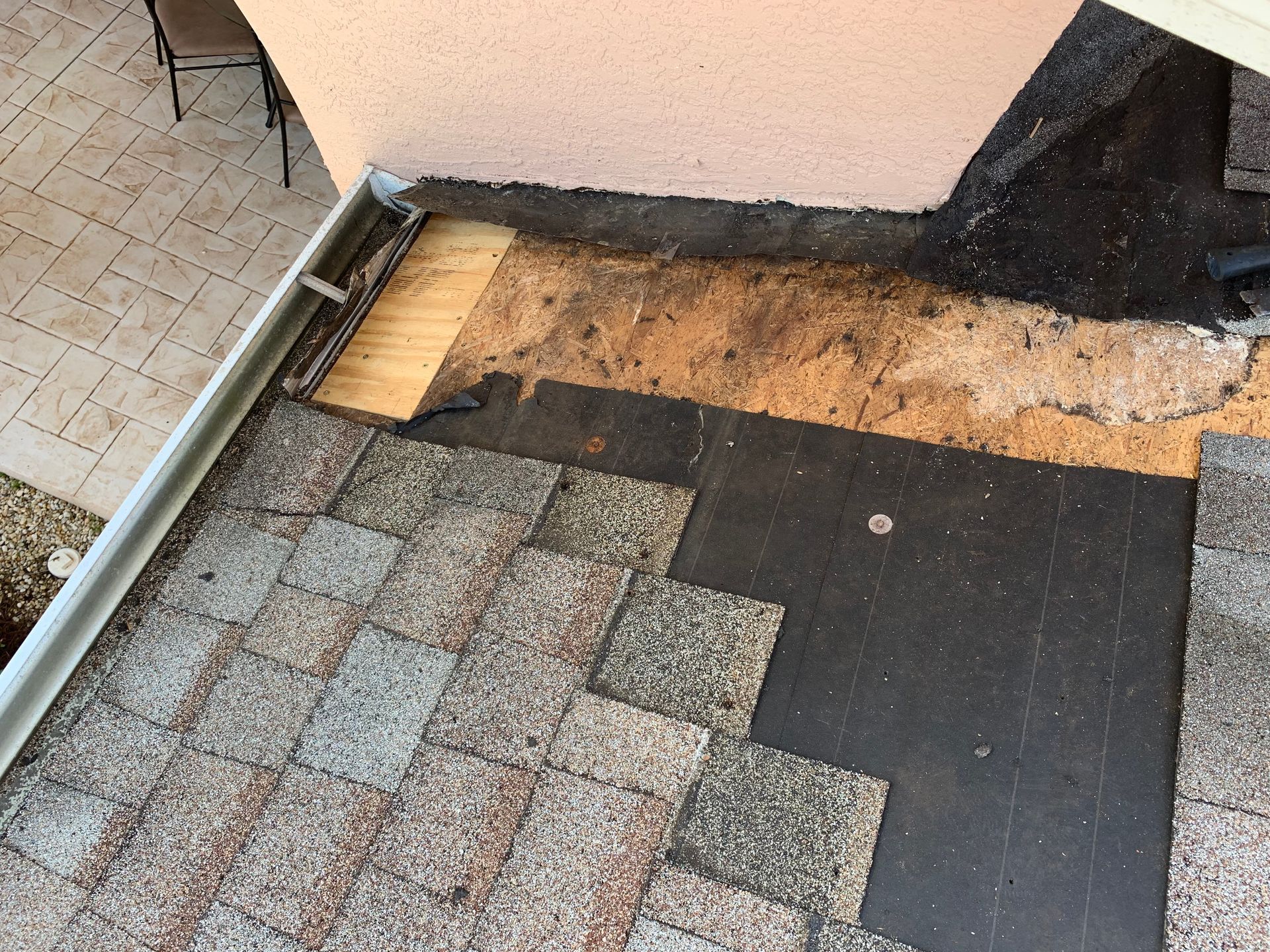 Damaged roof edge with exposed wood and missing shingles beside a tiled walkway