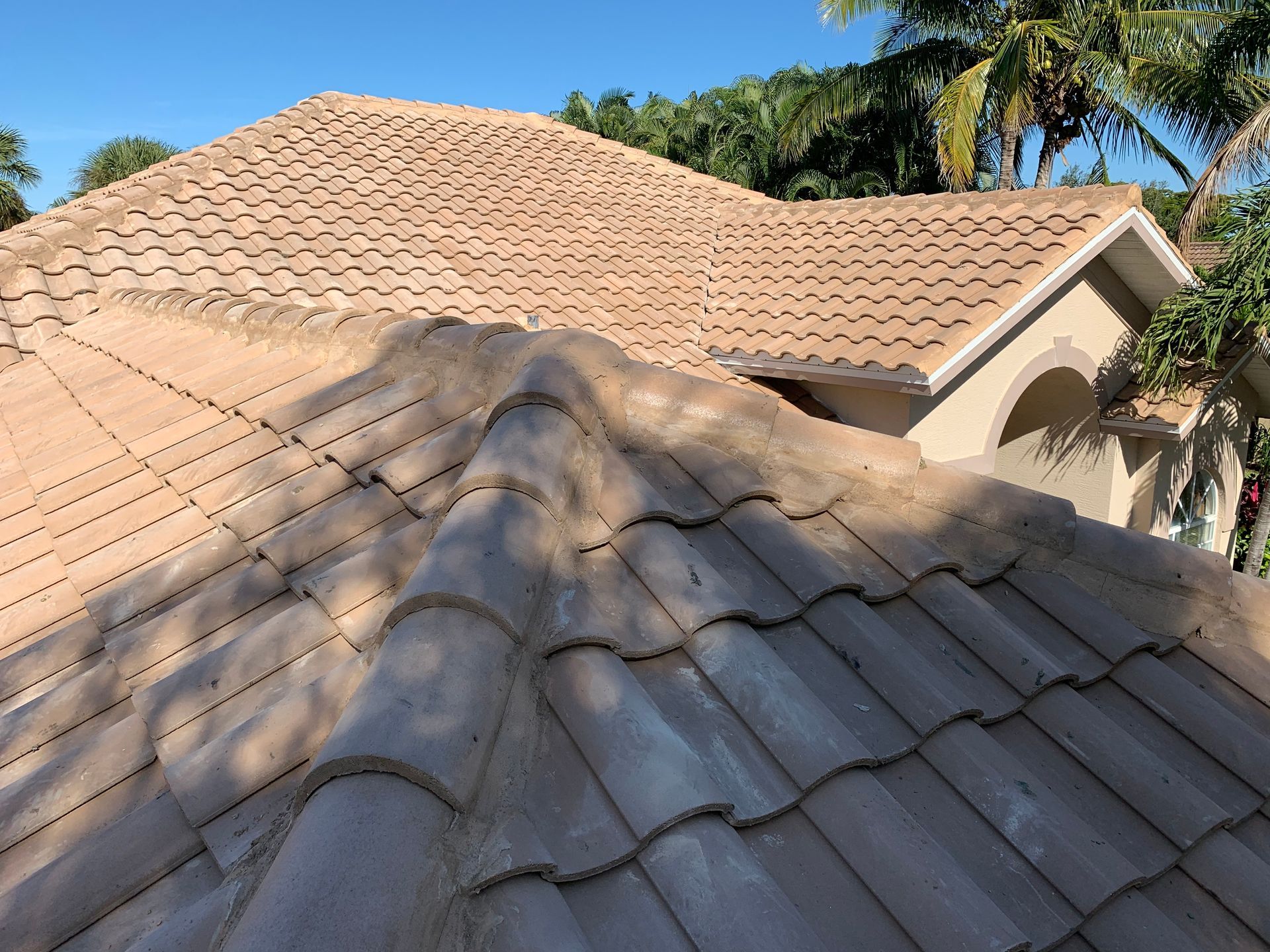 Sunlit terracotta roof tiles with shadowed ridges beside a cream-colored house and blue sky