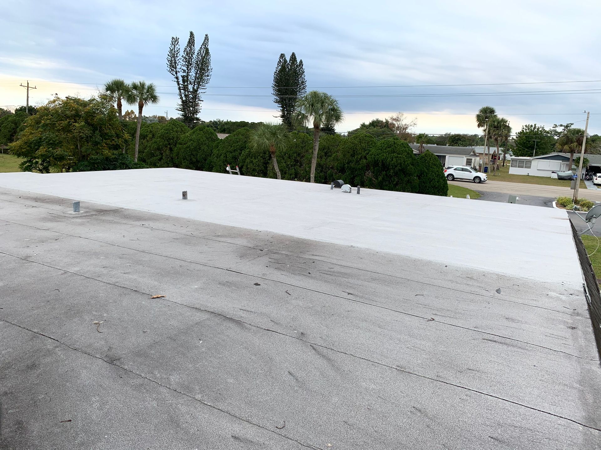 Flat white rooftop with trees and parked cars in the background under a cloudy sky