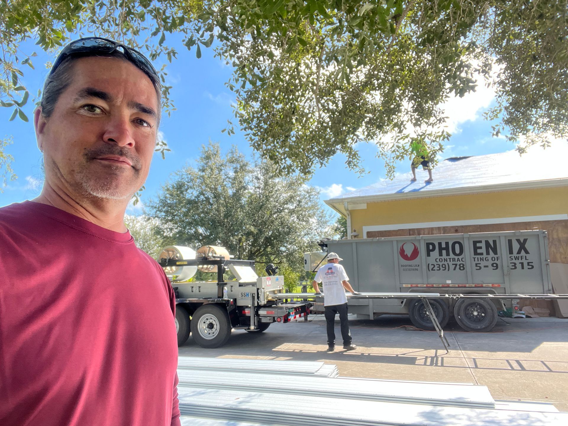 Man in red shirt taking selfie beside a Phoenix moving truck and another worker under a tree.