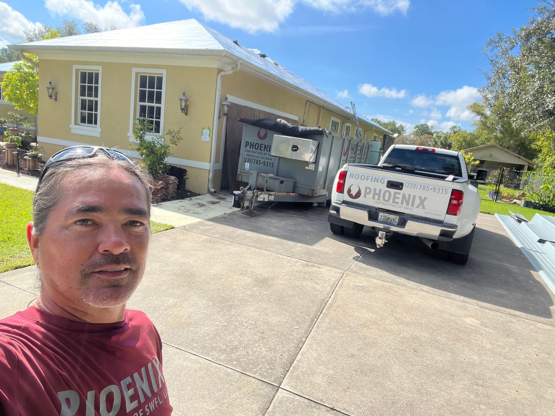 Man taking a selfie in a driveway with two Phoenix service vans outside a yellow house