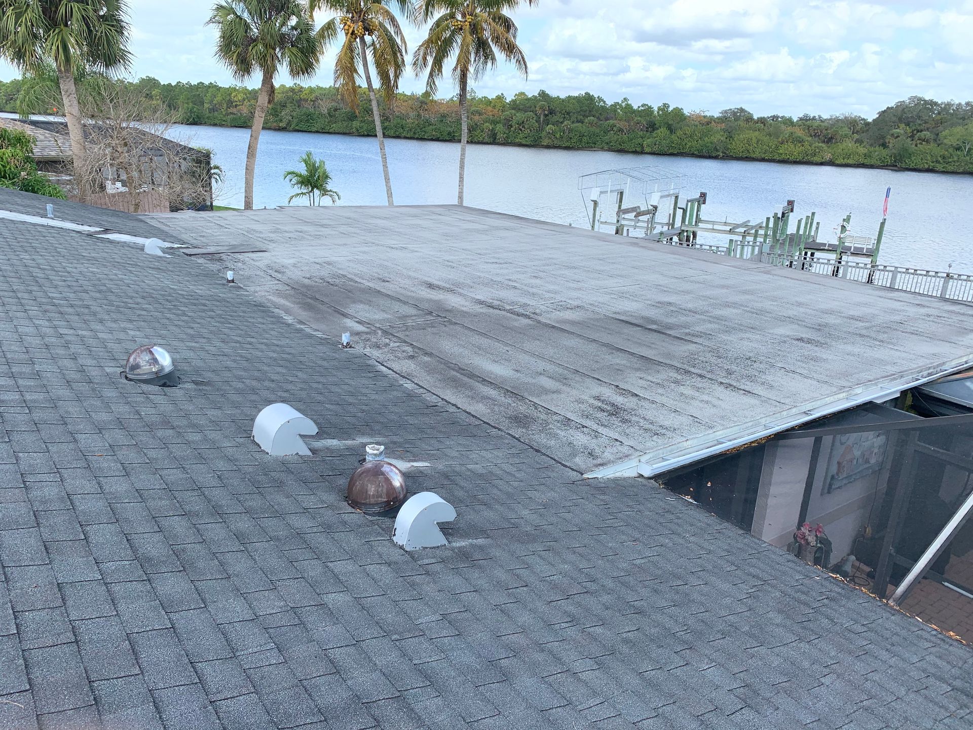 Rooftop overlooking a lake, with white domed vents and patio chairs near palm trees and a stone wall.