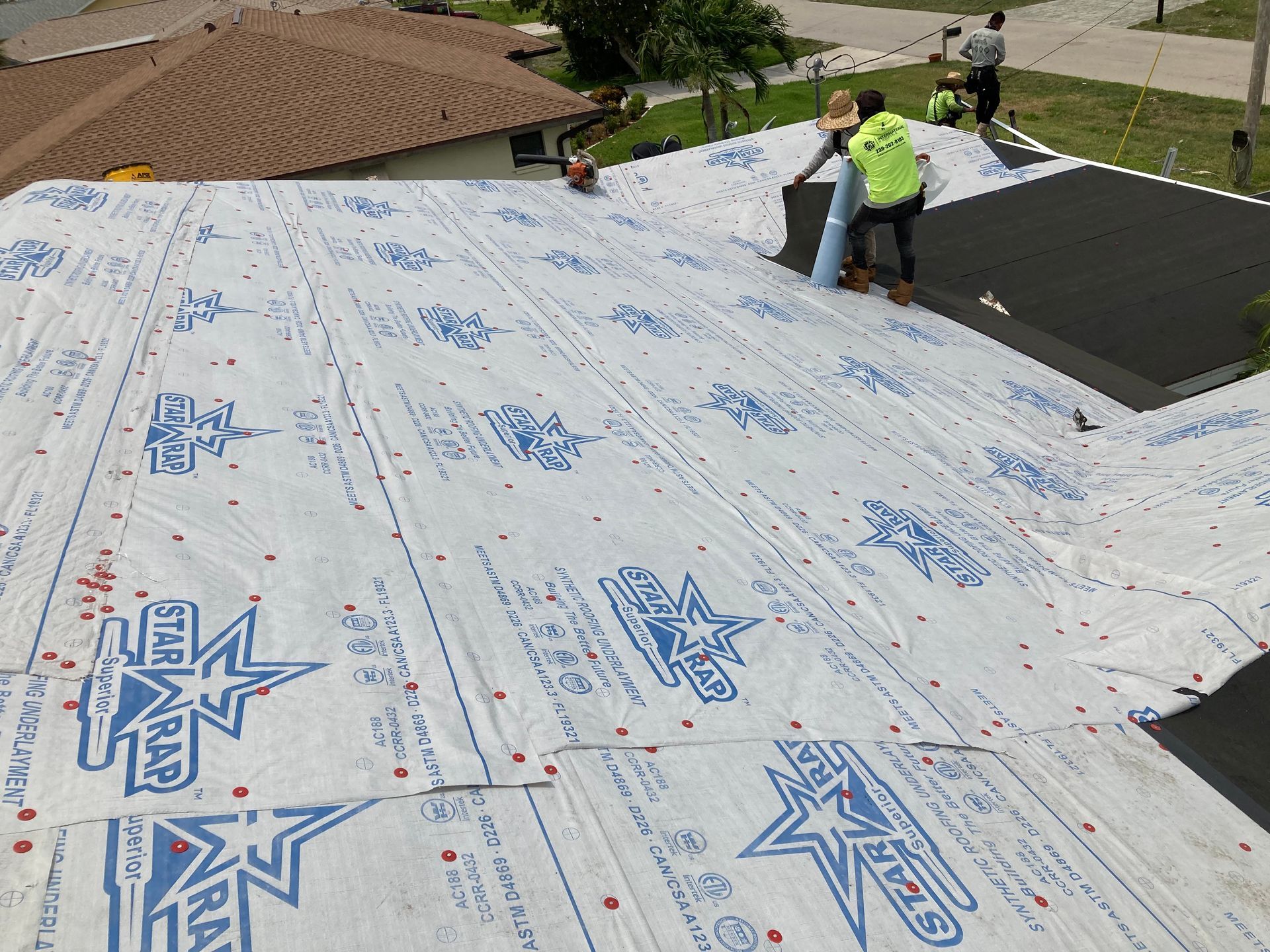 Workers covering a roof with white underlayment and a black section on the right.