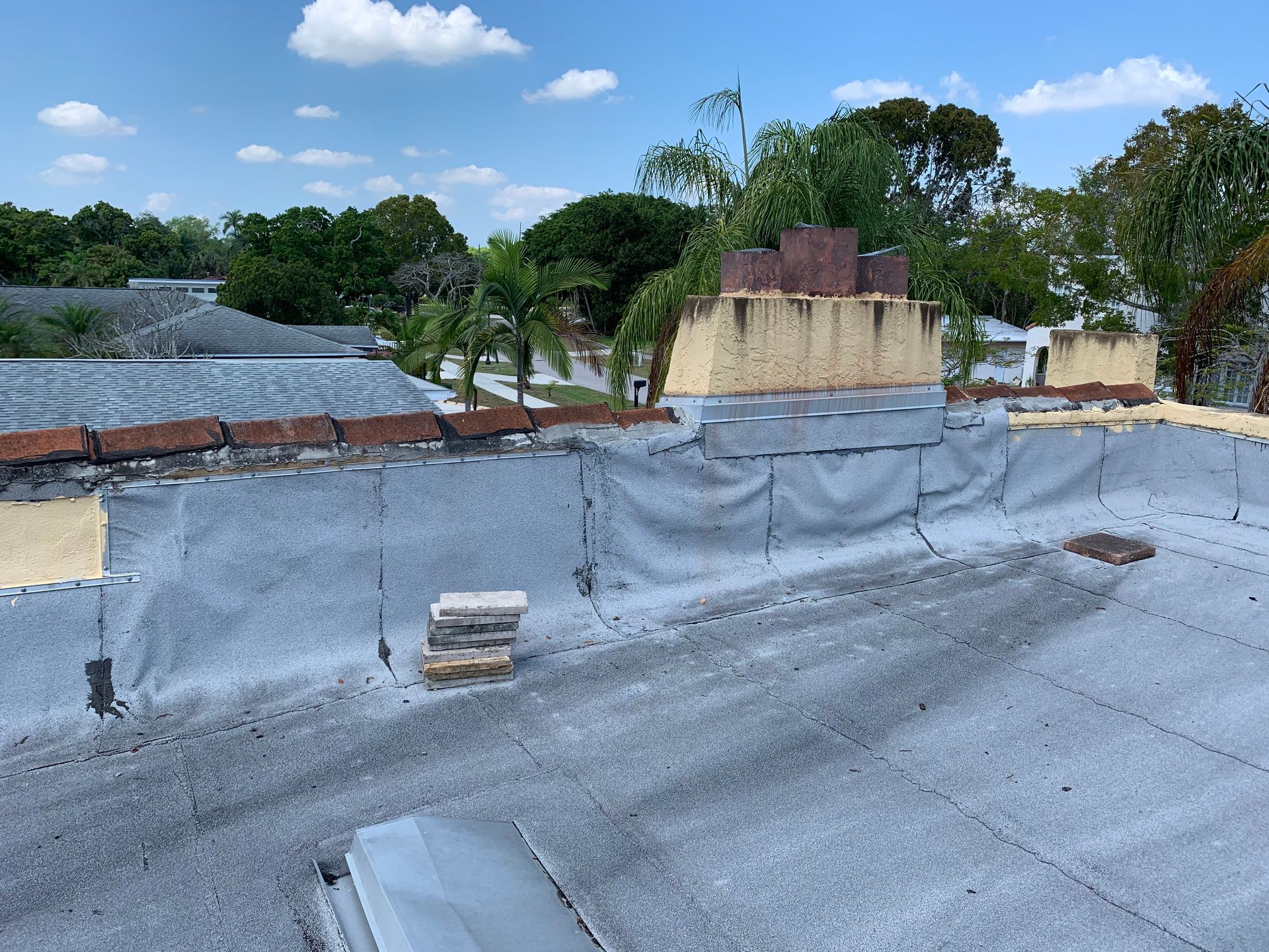 Roof under repair with gray waterproofing membrane, low brick wall, and trees under a blue sky