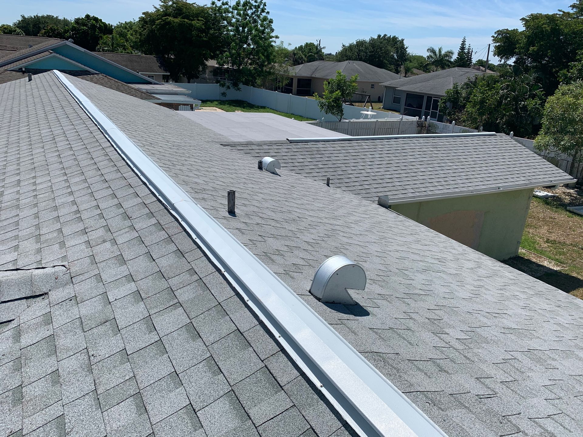 Flat gray roof with vents and ridge trim in a suburban neighborhood under a clear sky