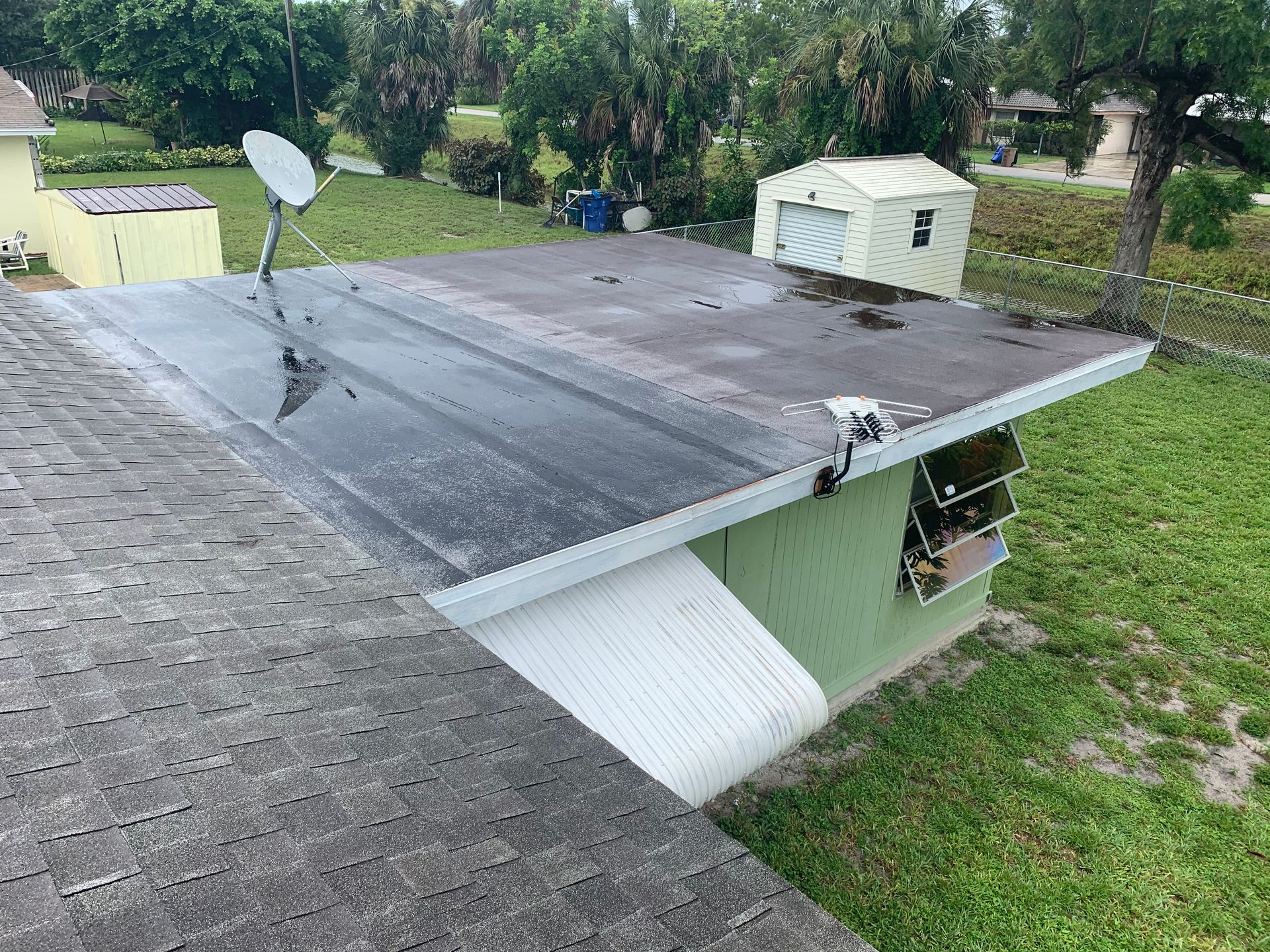 Small green shed with a black slanted roof and satellite dish in a grassy backyard