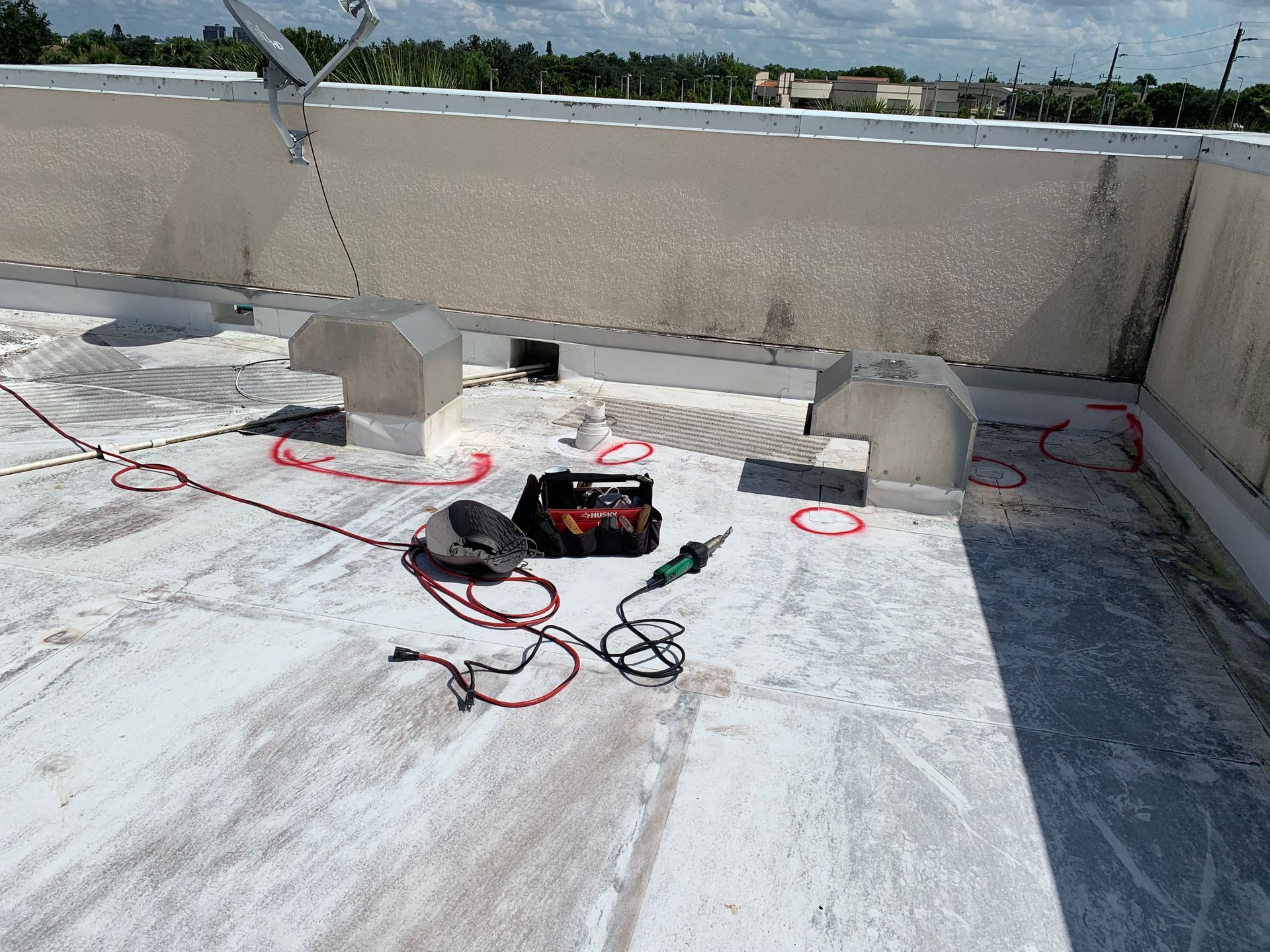 Rooftop with HVAC units, coiled cables, and a black tool bag on a white membrane roof under a blue sky.