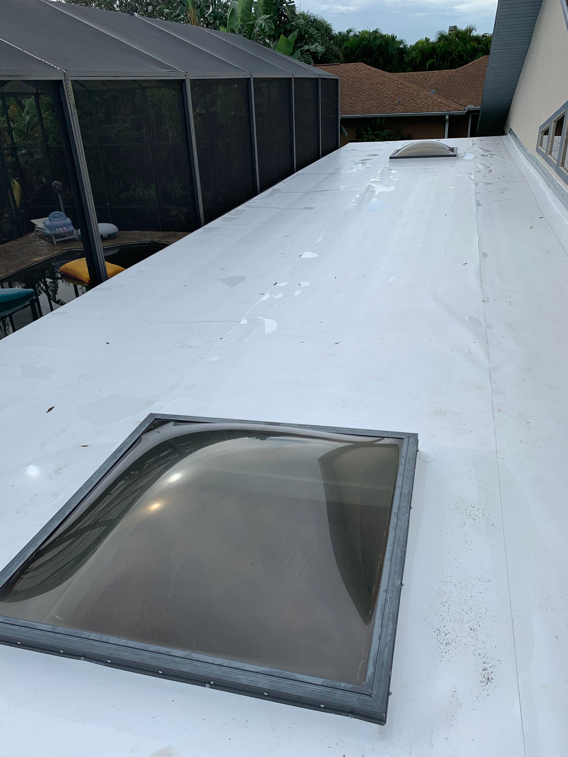 Flat white roof with two skylights beside a screened patio and neighboring houses