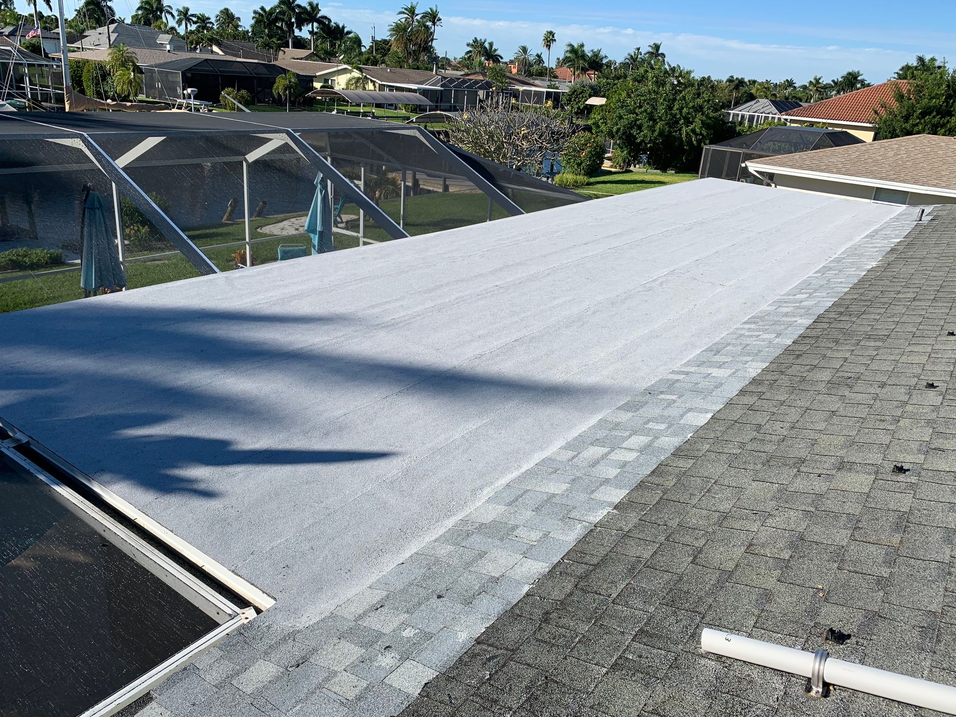 Rooftop covered with white solar panel sheets beside black mesh fencing under a clear sky