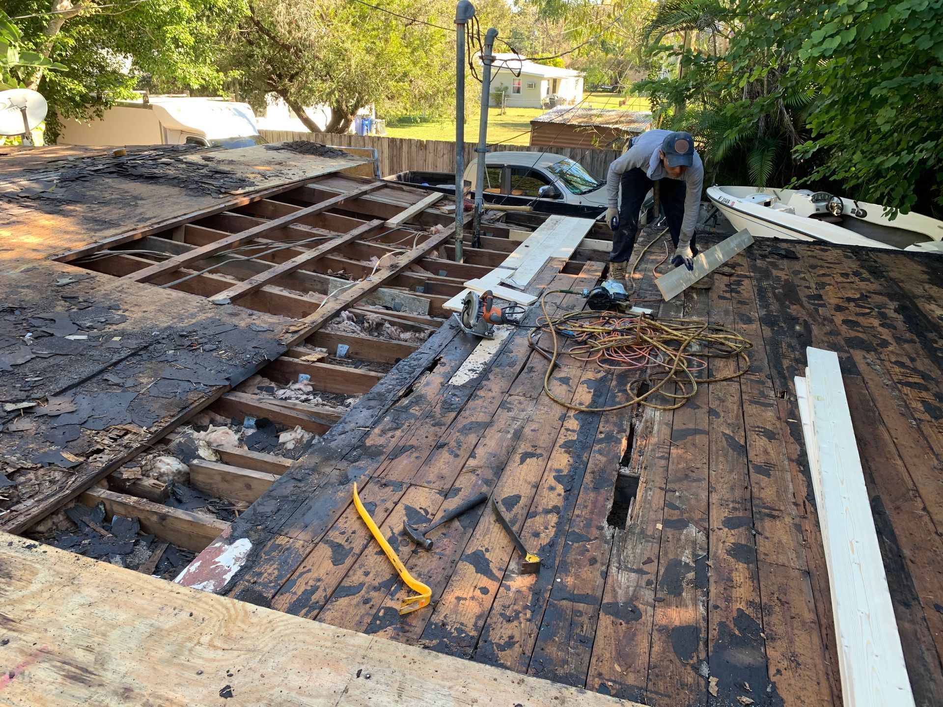 Roof under repair, with workers removing old shingles and exposed wooden decking visible.