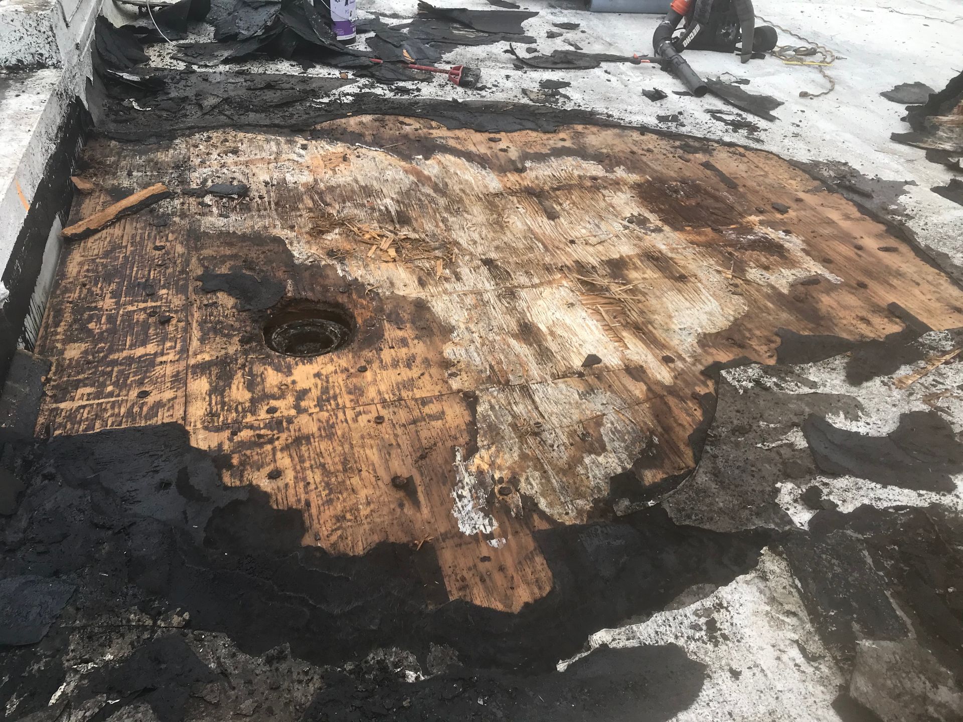 Burned, charred plywood or roofing debris with a circular hole amid snow and ash