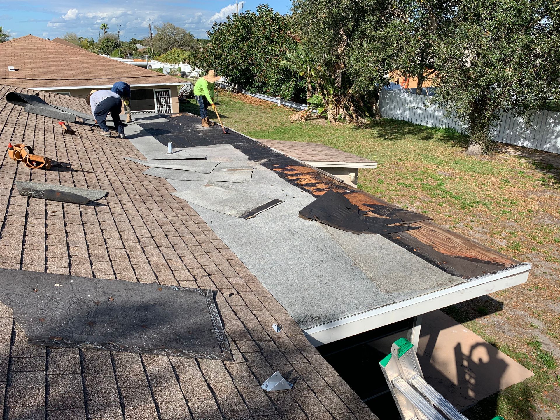 Workers installing roofing on a house, with gray underlayment and dark shingles along a sloped roof.