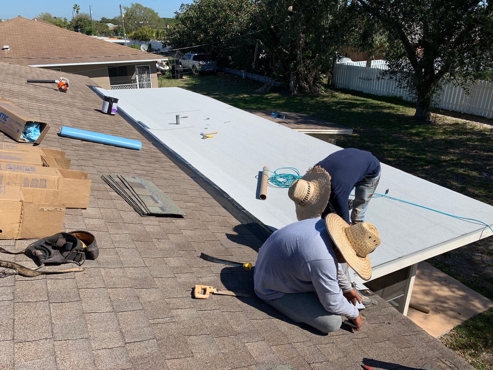 Workers installing a large white rooftop panel on a sunny roof