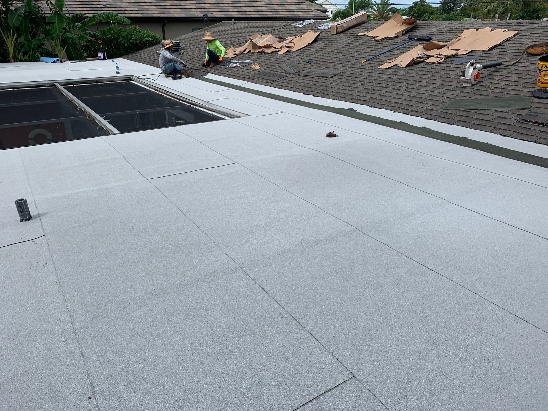 Flat rooftop under construction with gray roofing panels and workers in the background